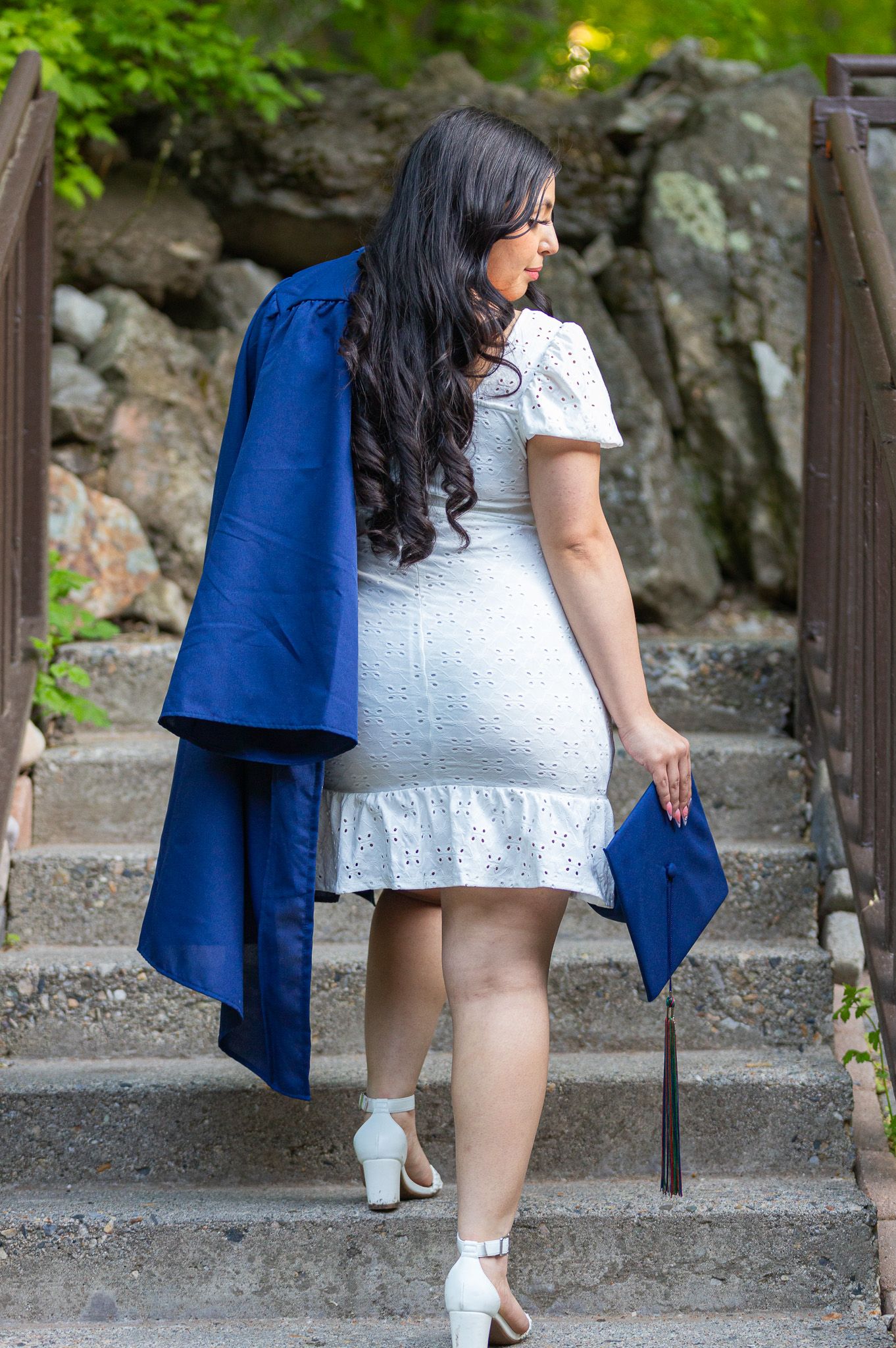 Graduate in white lace dress and blue graduation gown climbing stone steps in Utah.