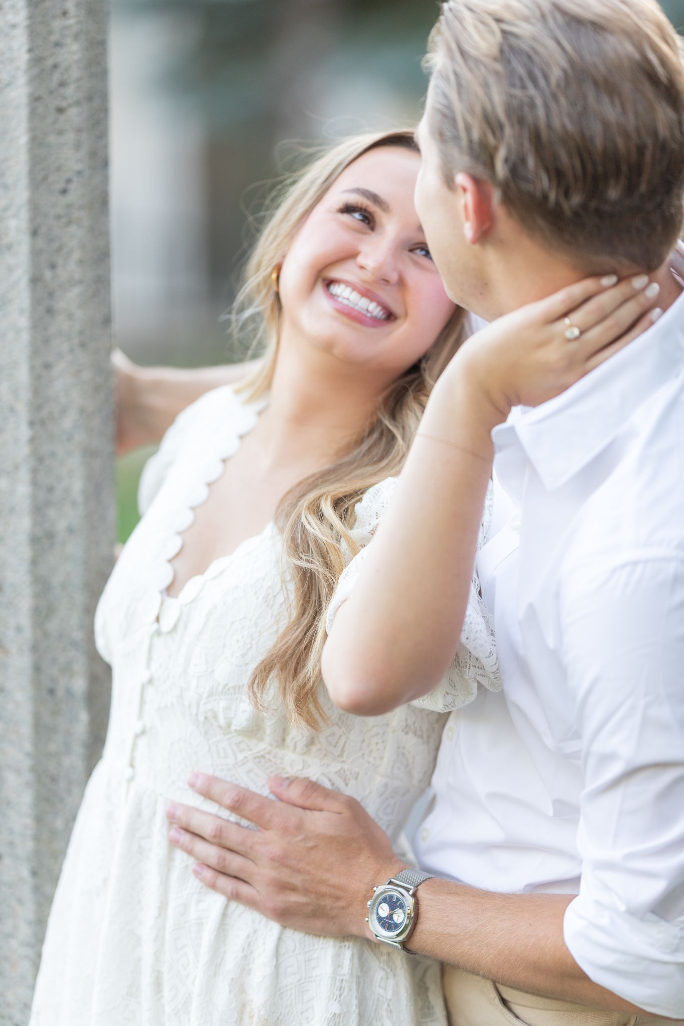 Romantic couple in white clothing poses intimately against light colored backdrop.