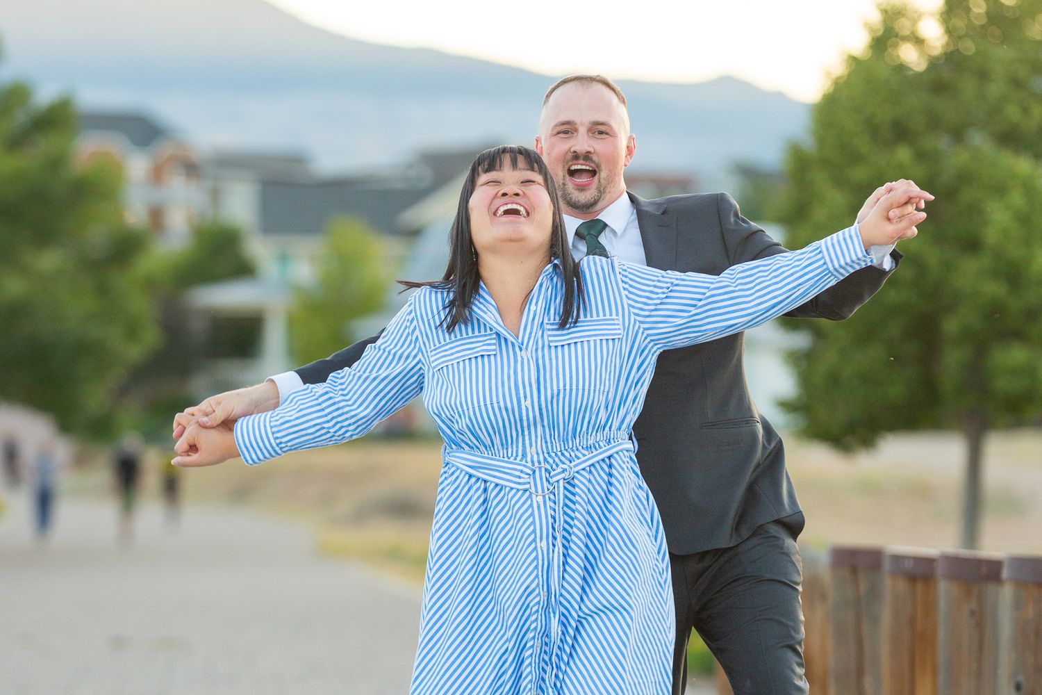 Joyful moment captured on boardwalk with couple in formal attire against mountain scenery.