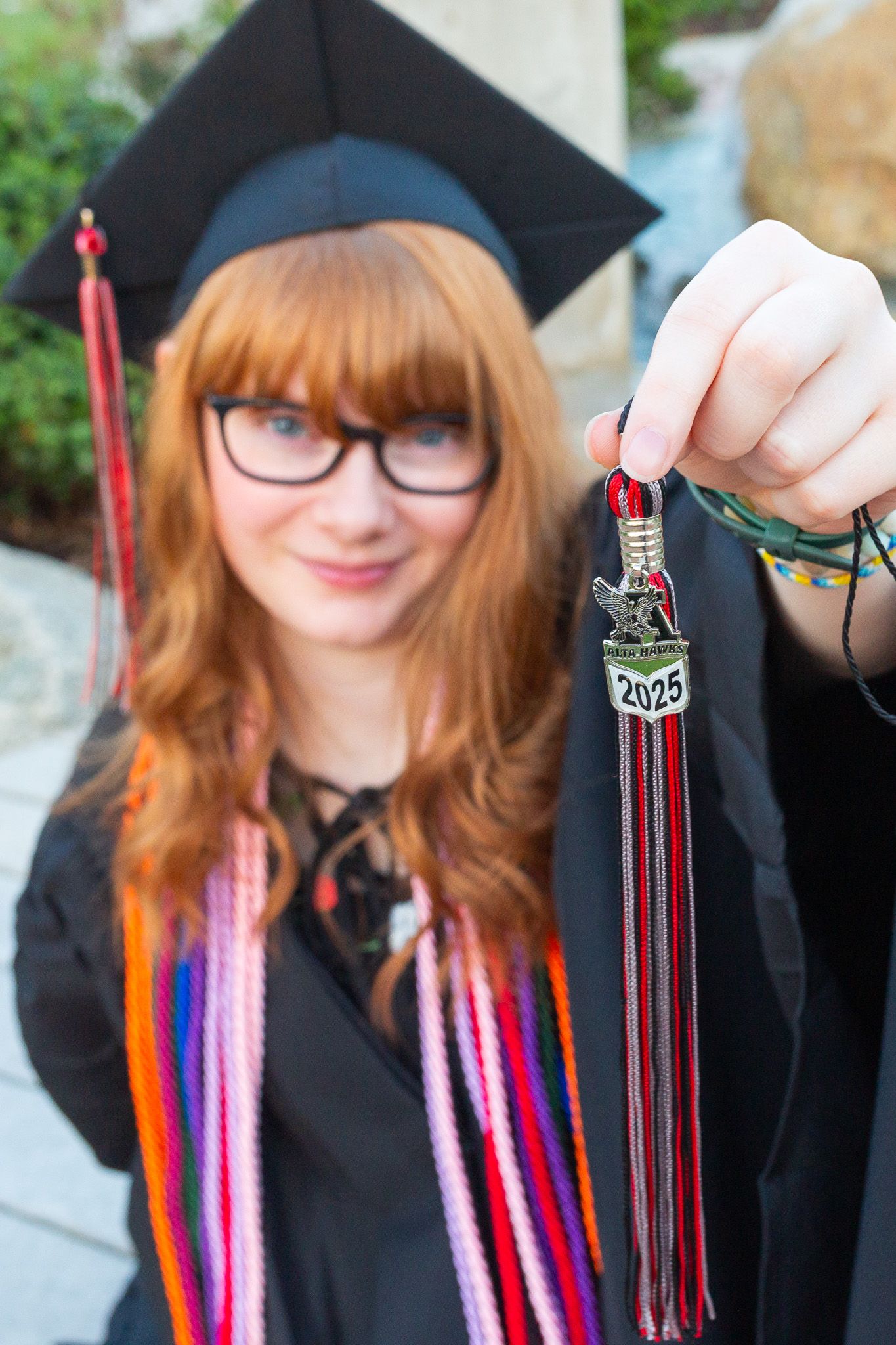 Graduate in cap and gown with red tassels holds up Class of 2025 for a Sandy, UT high school.