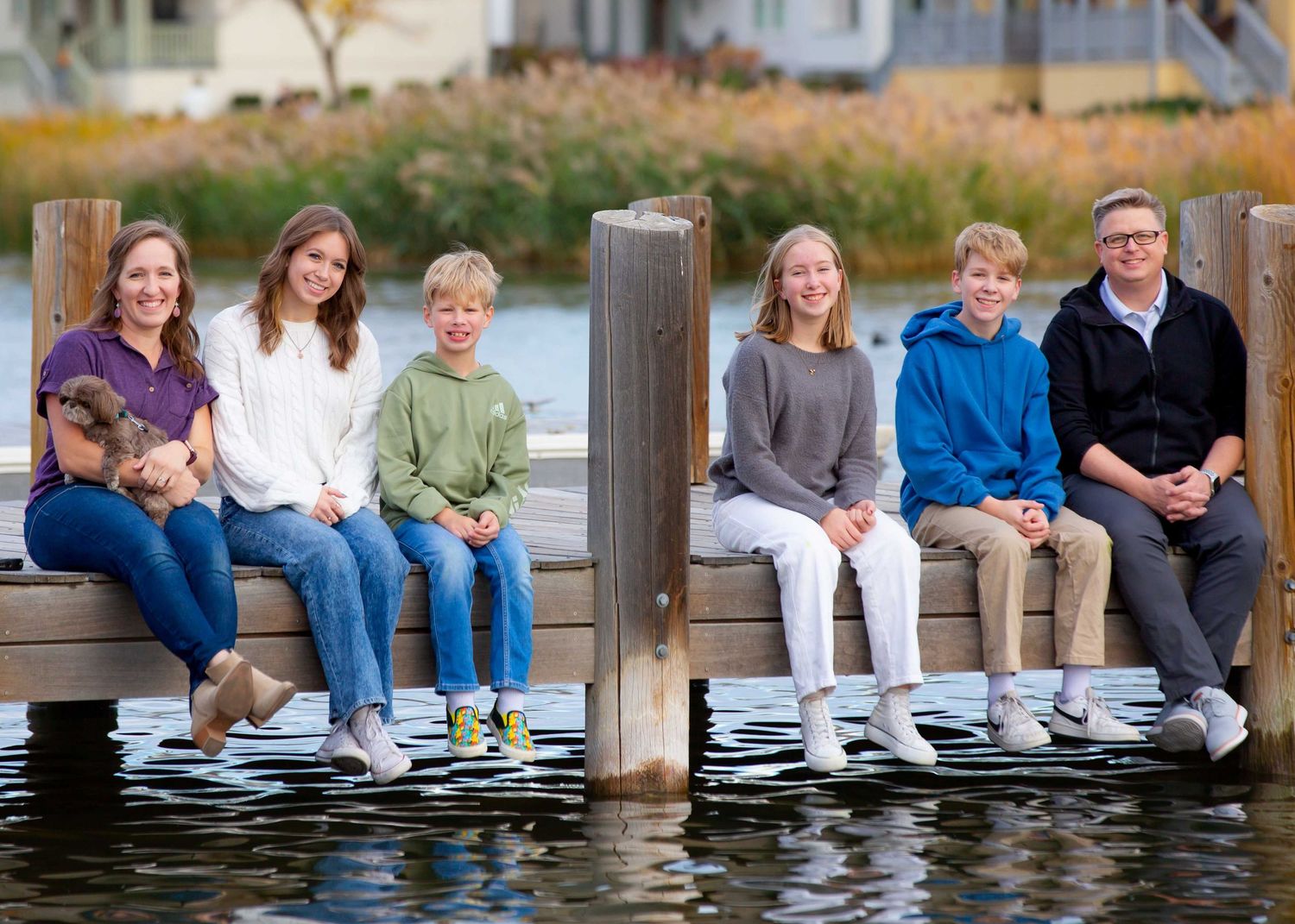 Group of people sitting together on a wooden pier over calm water reflecting the late afternoon sunlight.