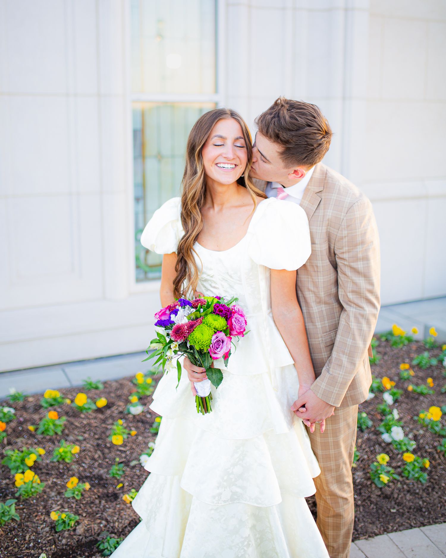 Couple in wedding attire sharing moment among colorful garden flowers.