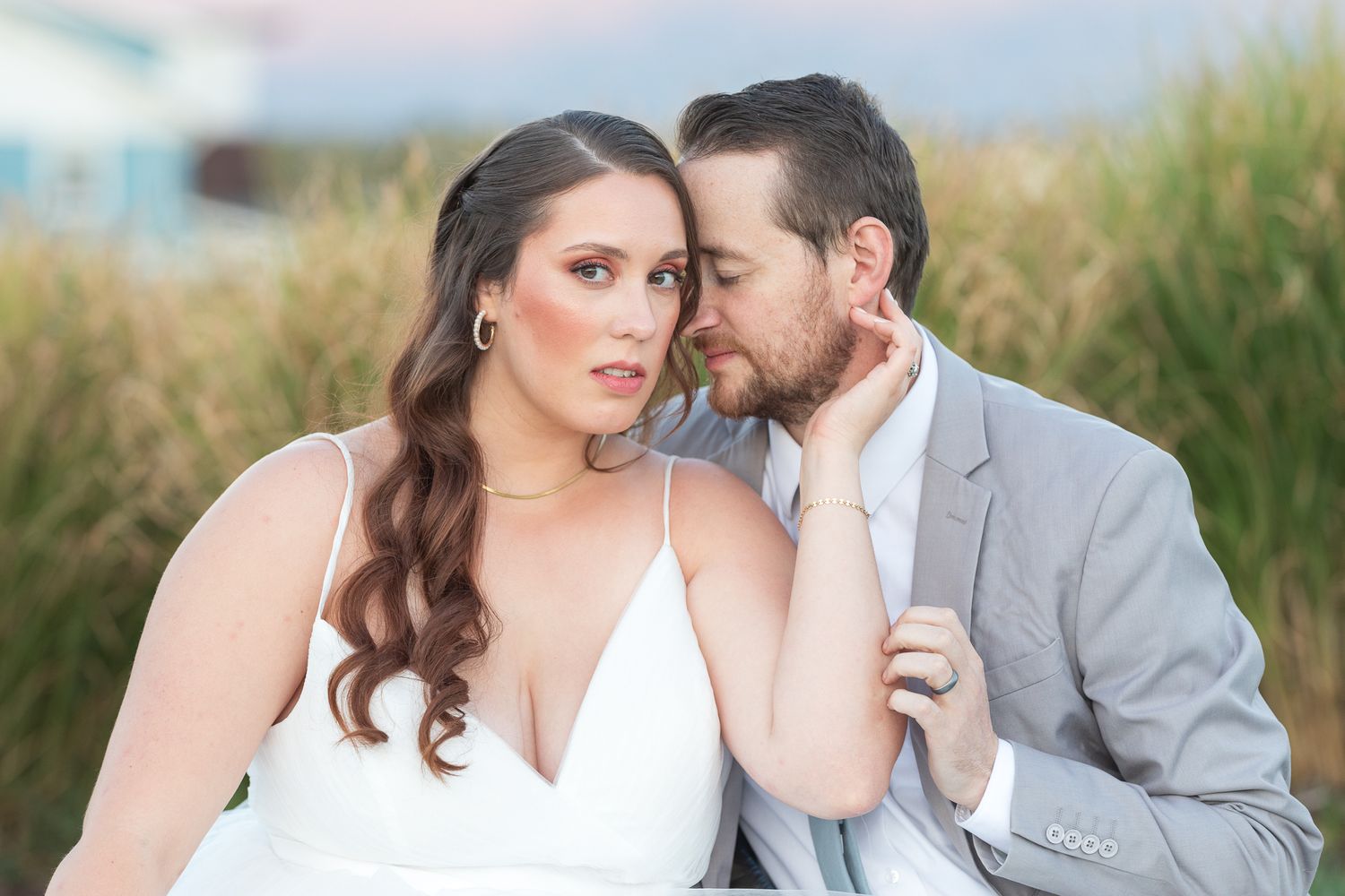 Romantic seaside portraits with couple among beach grass at sunset.