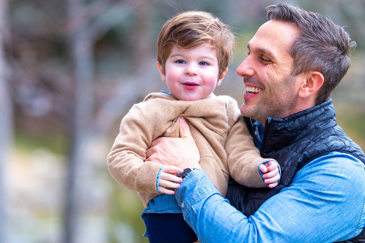 A parent and toddler share a joyful moment outdoors on a bright day.