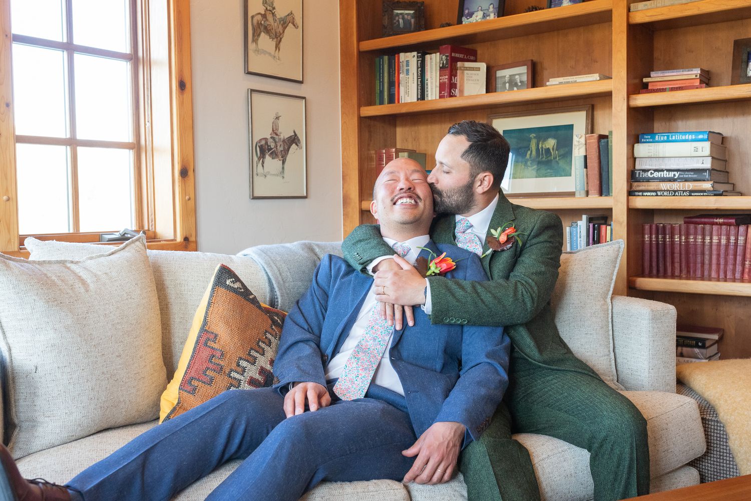 Two people share a tender moment while sitting on couch in home library setting.