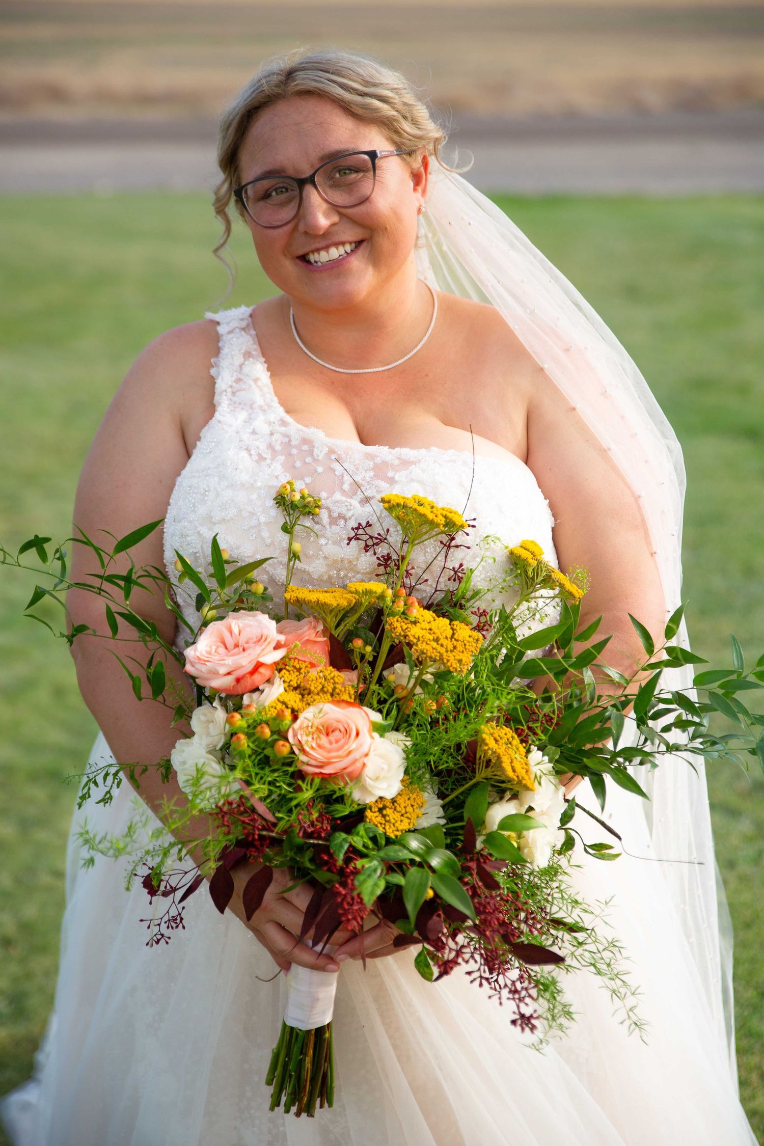 Radiant bride in white dress holding vibrant fall-colored wedding bouquet outdoors.