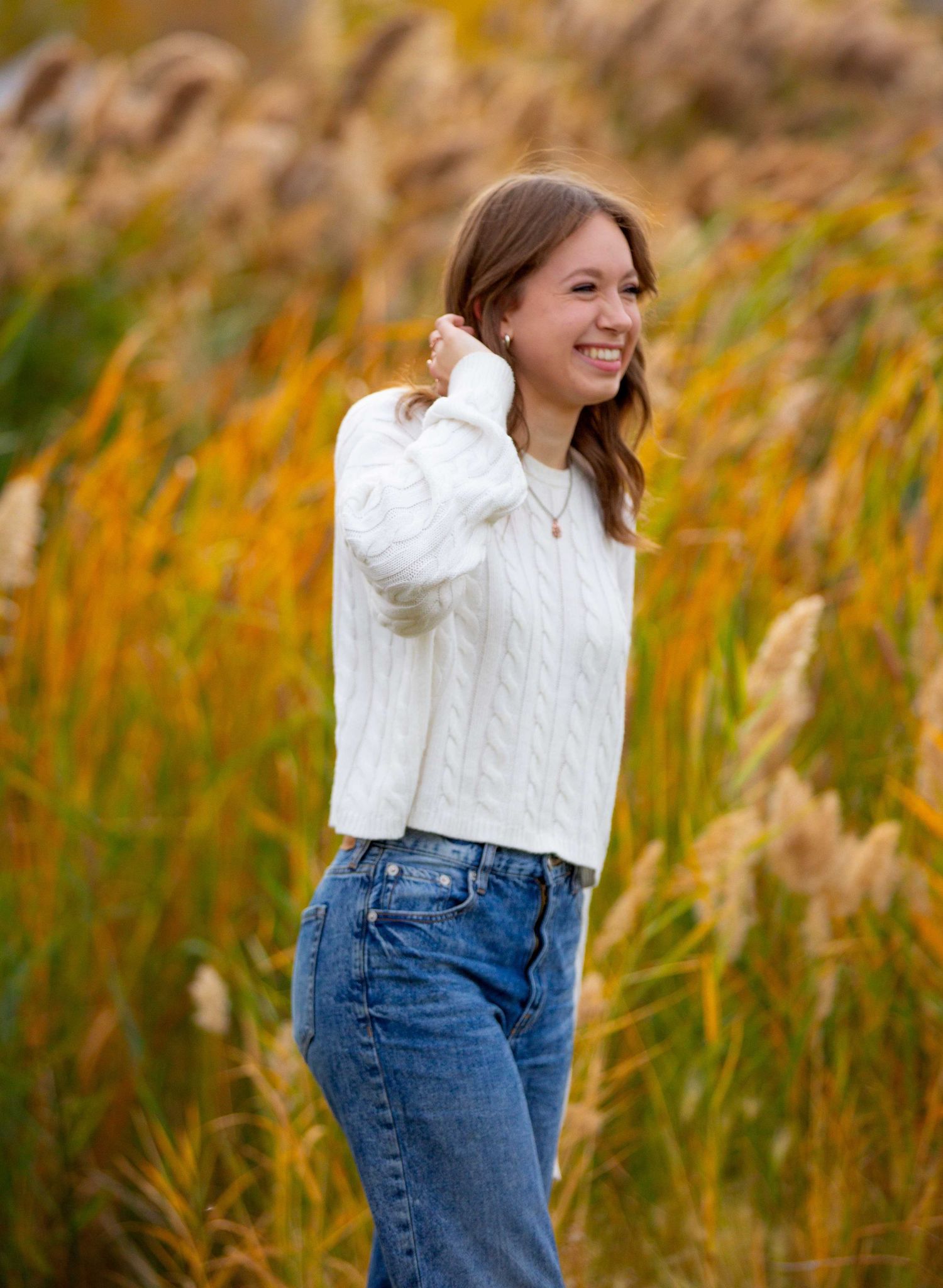 A series of outdoor portraits in a field of golden autumn grass showing someone in a white sweater and blue jeans.