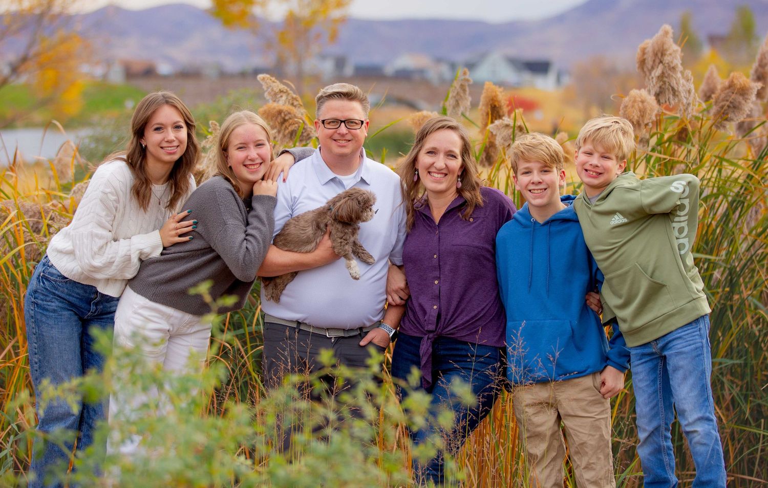 A group poses for a portrait in front of autumn mountains and foliage during golden hour.