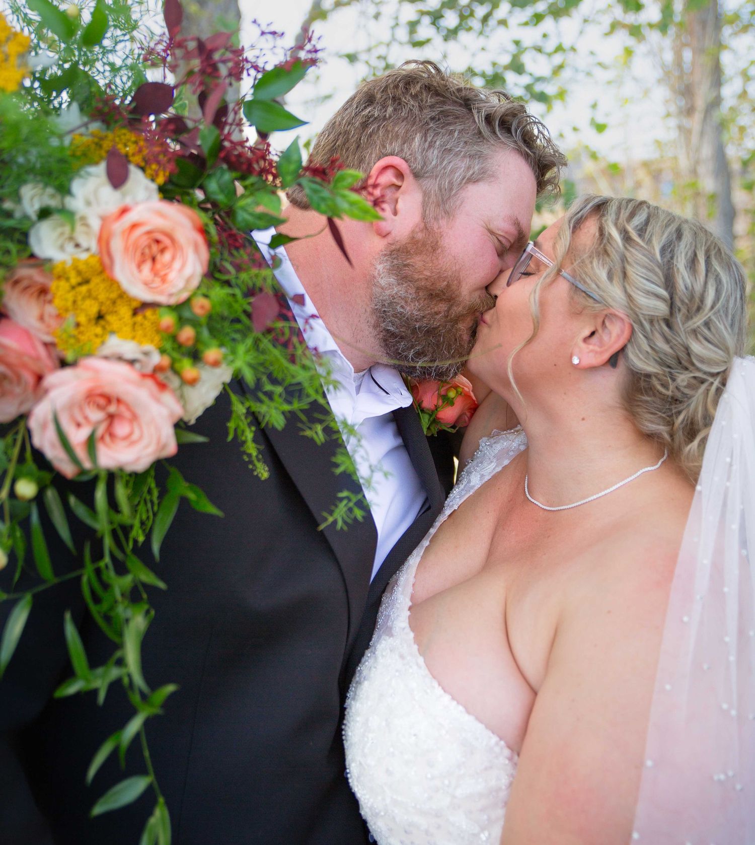 Bride and groom share a kiss next to colorful floral wedding arrangements.