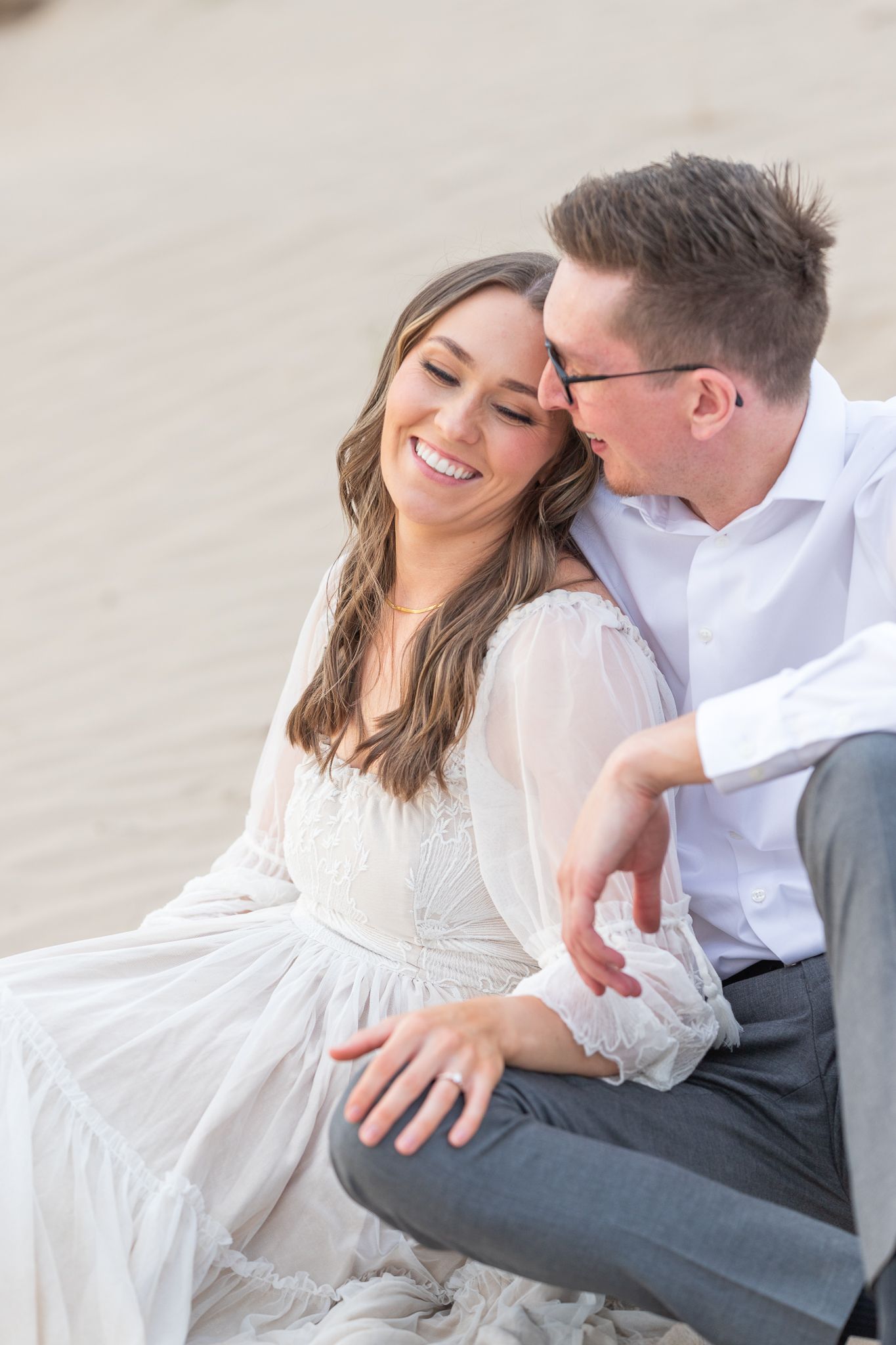 Couple shares intimate moment during casual engagement photo session against neutral wall.