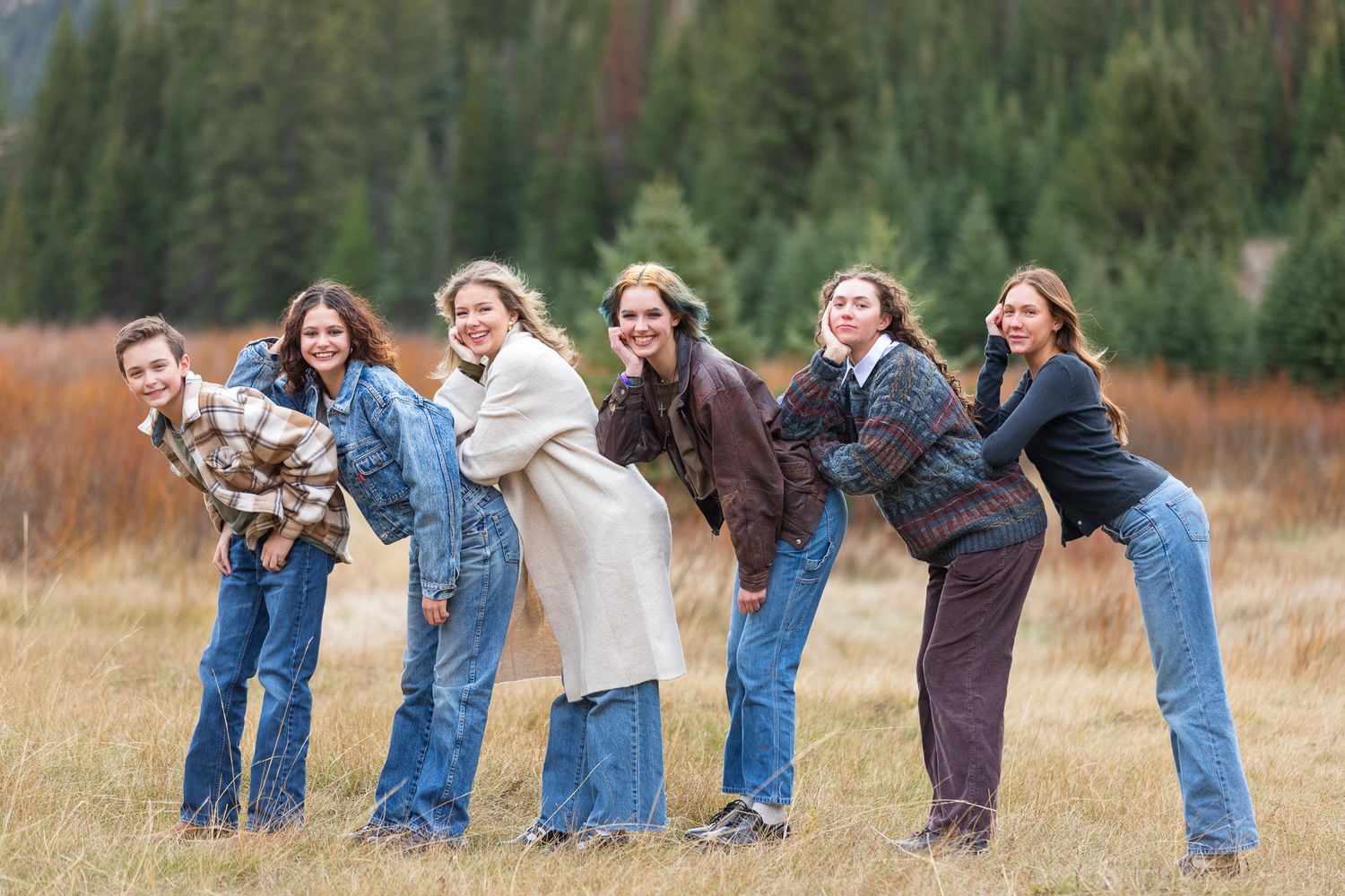 A playful family lined up in Big Cottonwood Canyon, Utah bends forward in a domino effect pose wearing denim and casual clothing.