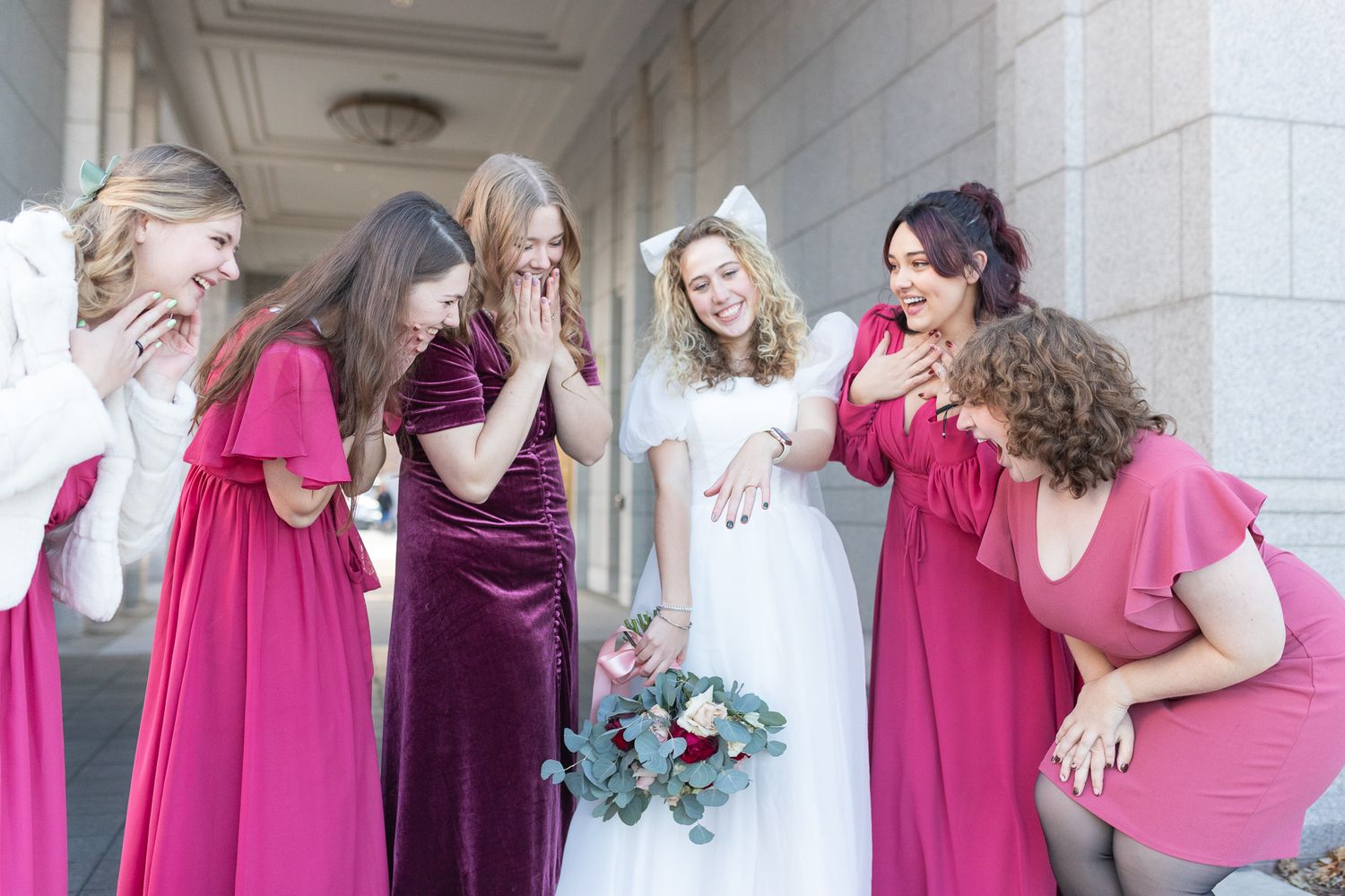 Bridal party shares emotional moment in marble hallway with bride holding blue and white bouquet.