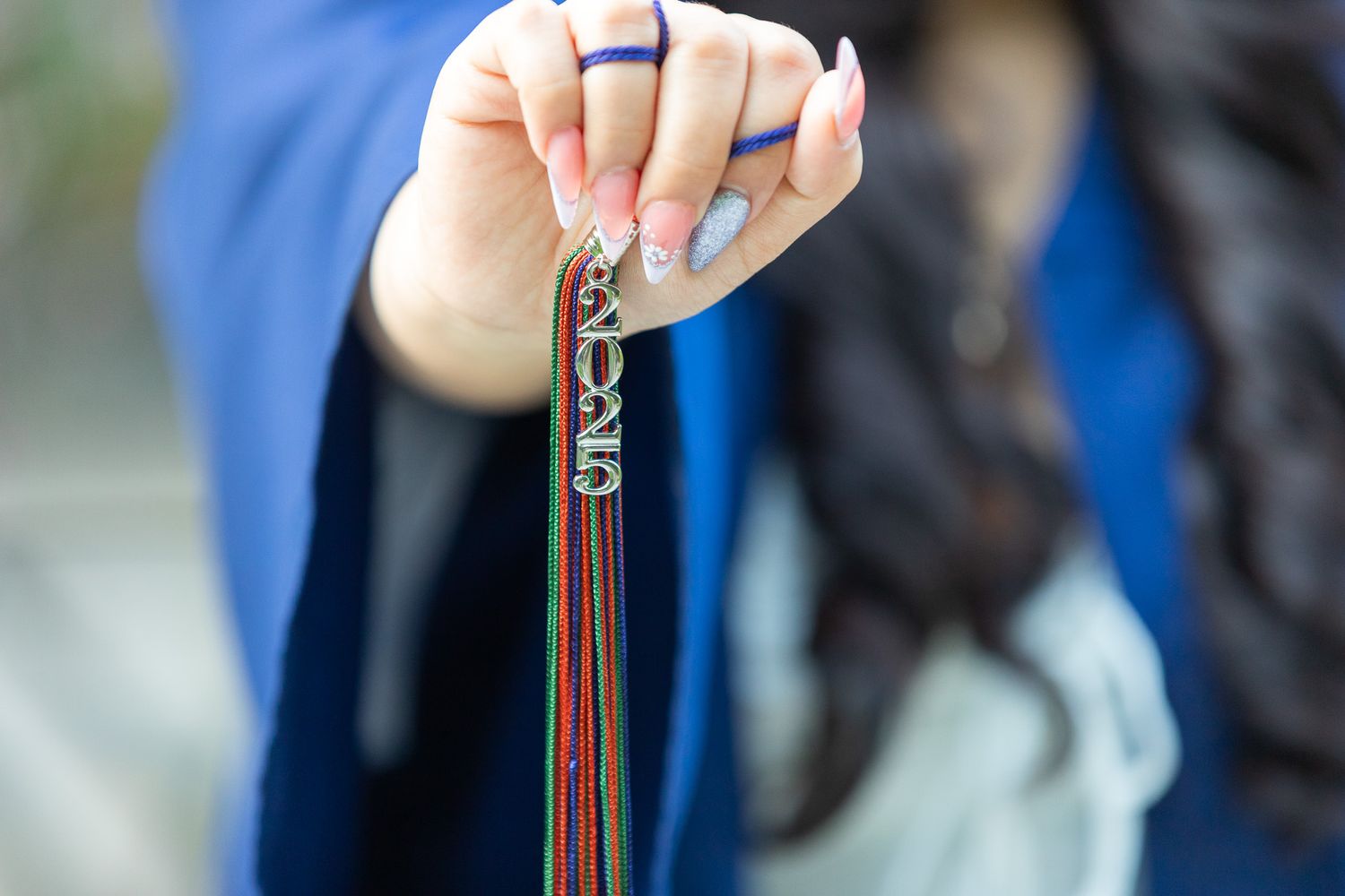 A hand holds a colorful metallic keychain tassel or lanyard charm with beaded details against a blurred background.