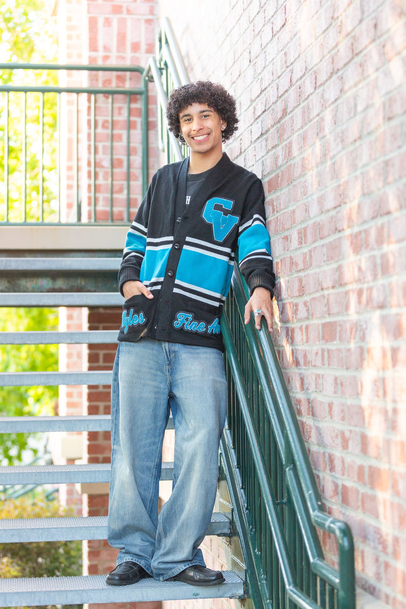 Student in blue and black varsity sweater and jeans stands on brick staircase with green railing.