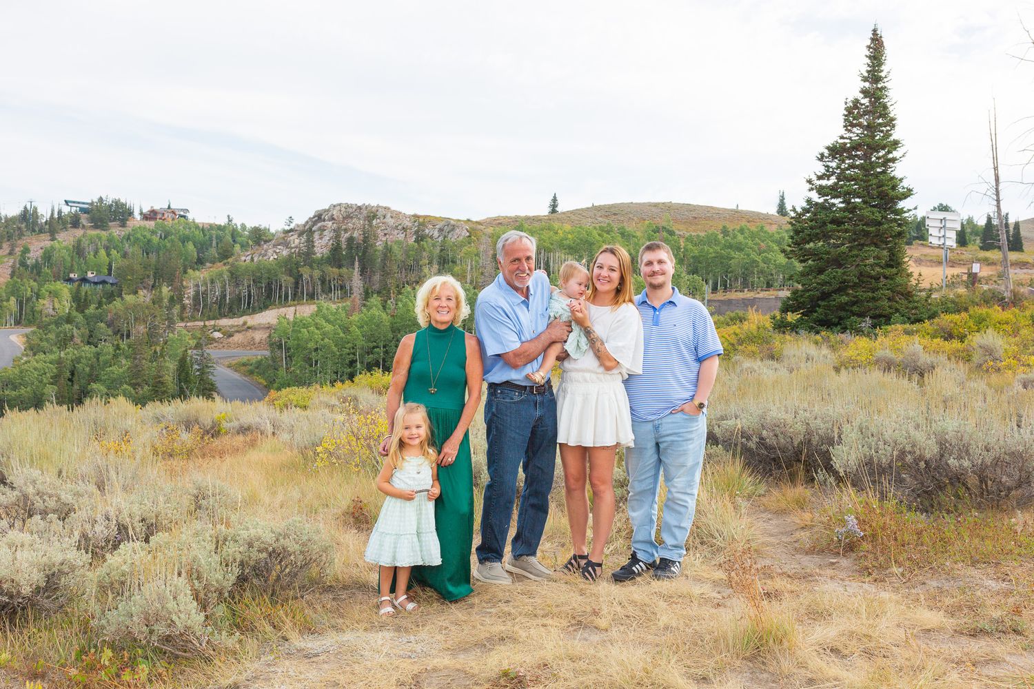 A family stands together on a mountain trail in Park City, Utah surrounded by sagebrush and evergreen trees in the autumn landscape.