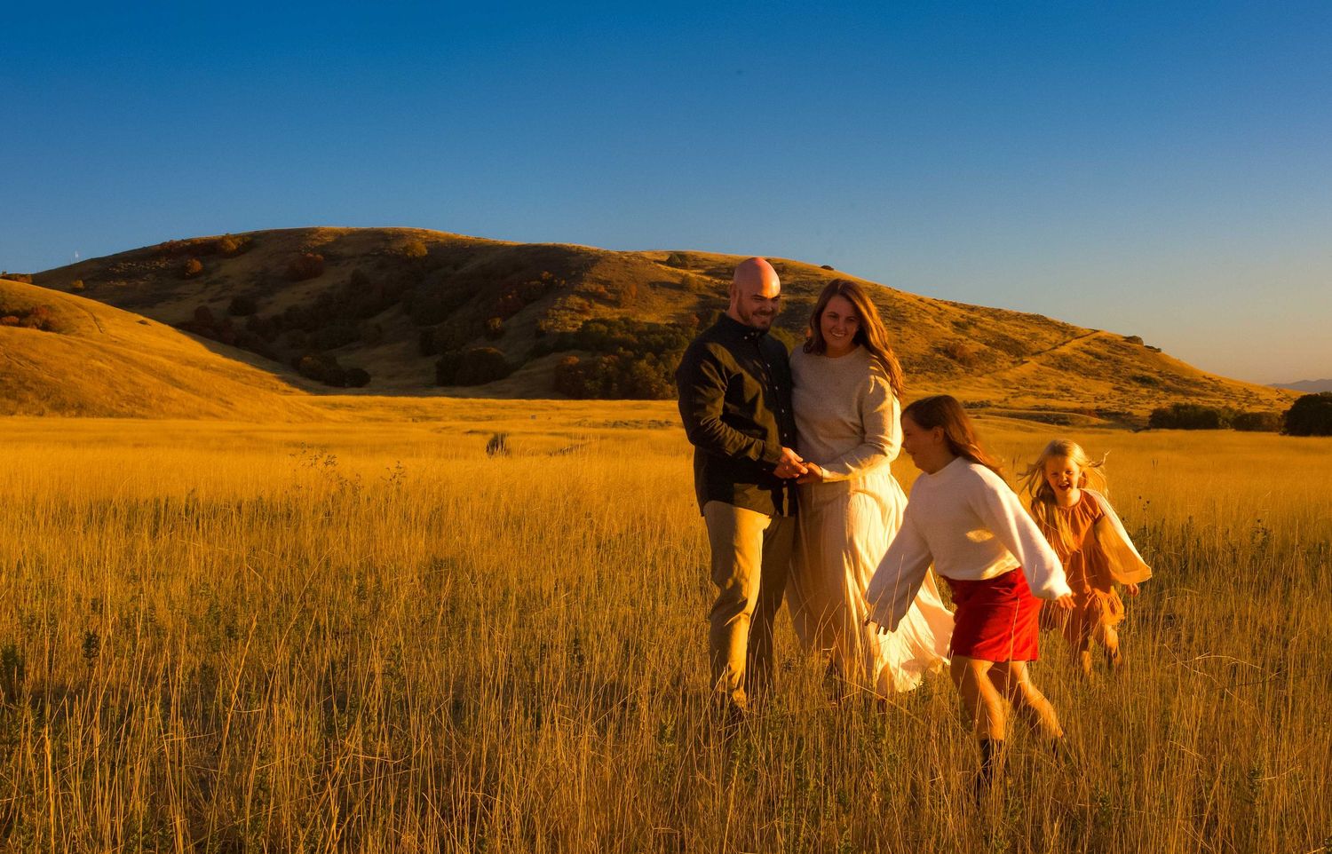 People walk through a golden prairie field at sunset with mountains visible in the distance creating a scenic landscape.
