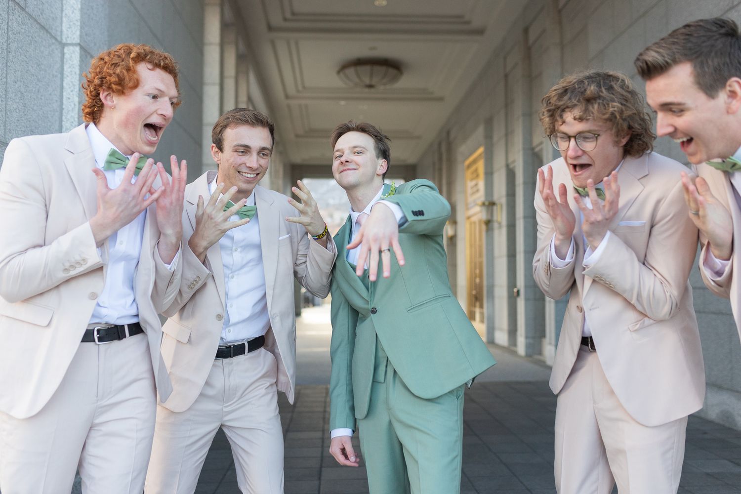 Groomsmen laugh and celebrate in light colored suits with one wearing mint green.