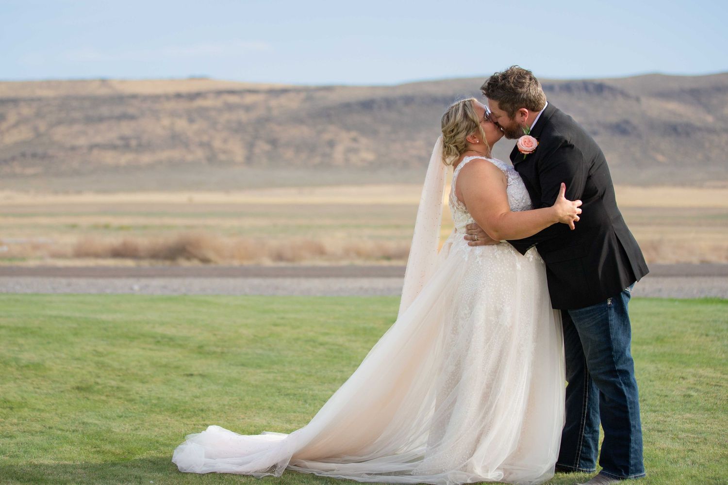 Newlyweds share a romantic moment in their wedding attire against a desert landscape.