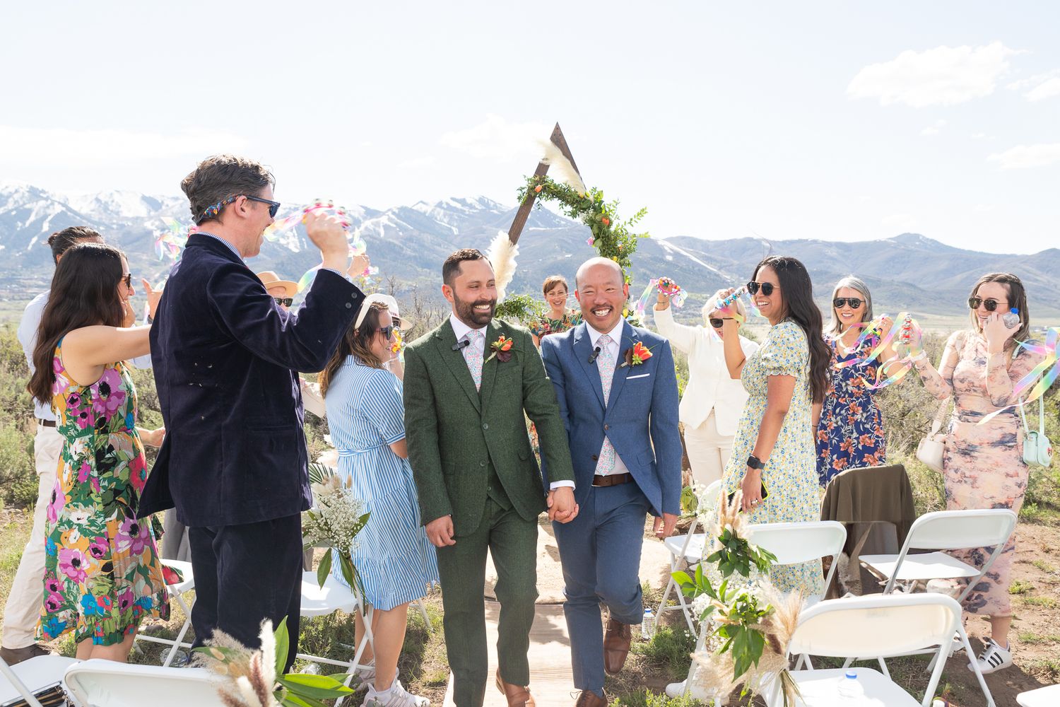Wedding ceremony celebration with guests cheering as couple walks down outdoor aisle with mountain backdrop.