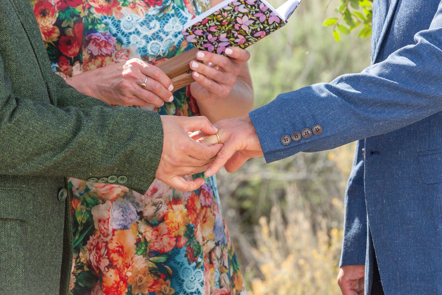 Couple exchanging rings during outdoor wedding ceremony with floral accents.
