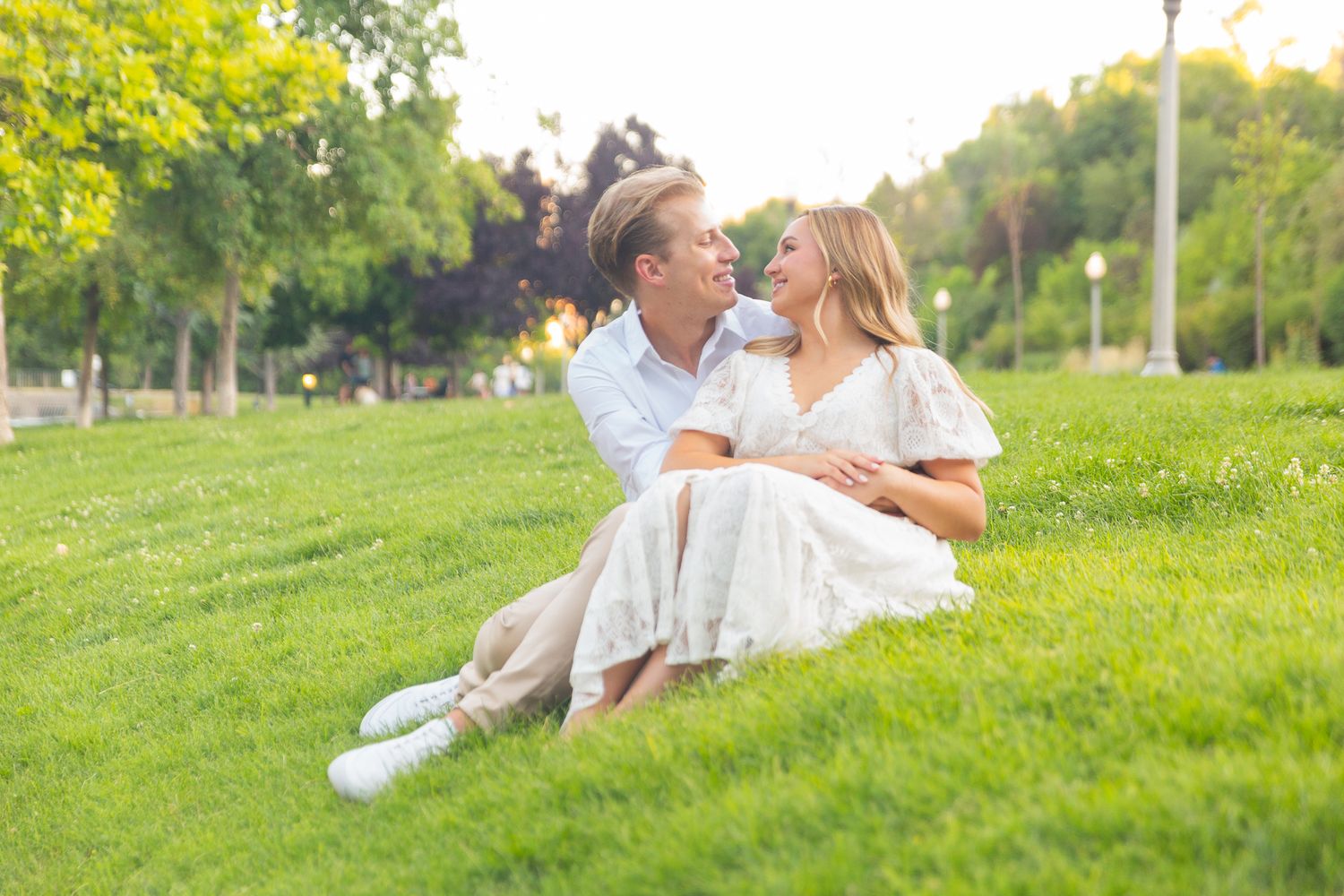 Couple relaxing on grassy hillside during golden hour photo session.