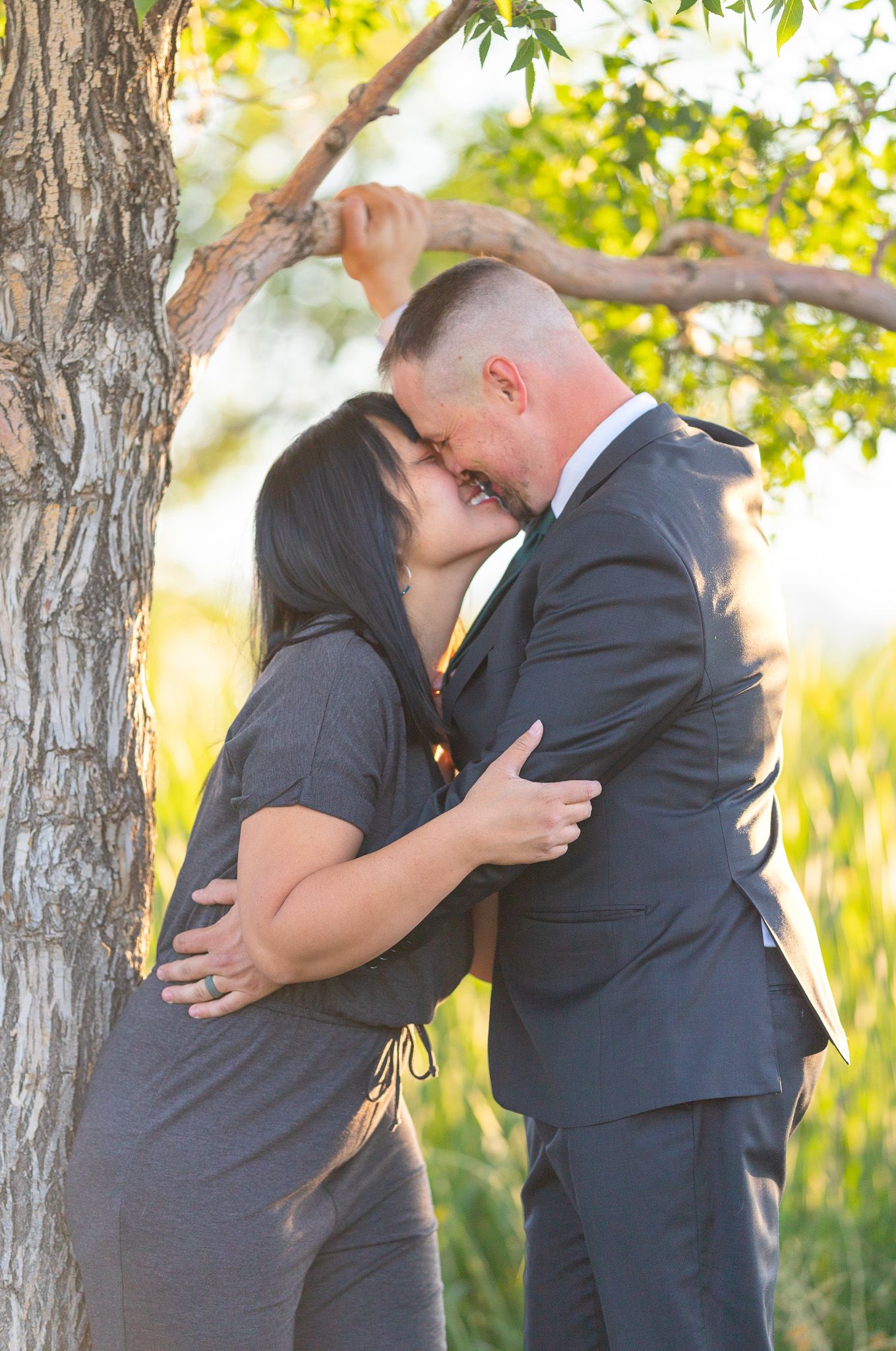 A romantic couple shares tender moments beneath trees during golden hour.