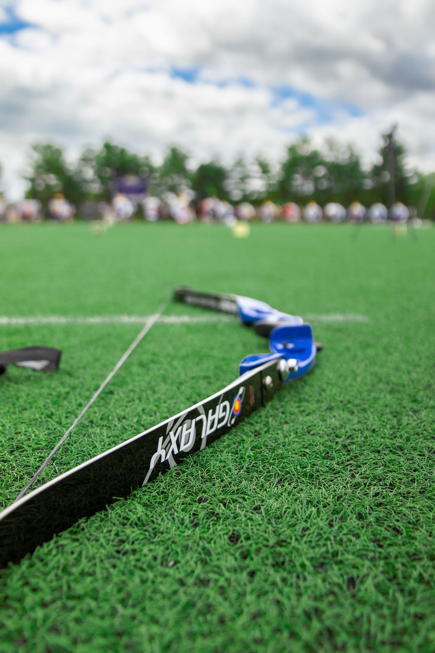 Close-up of a black and blue archery bow lying on green grass with soft focus background.