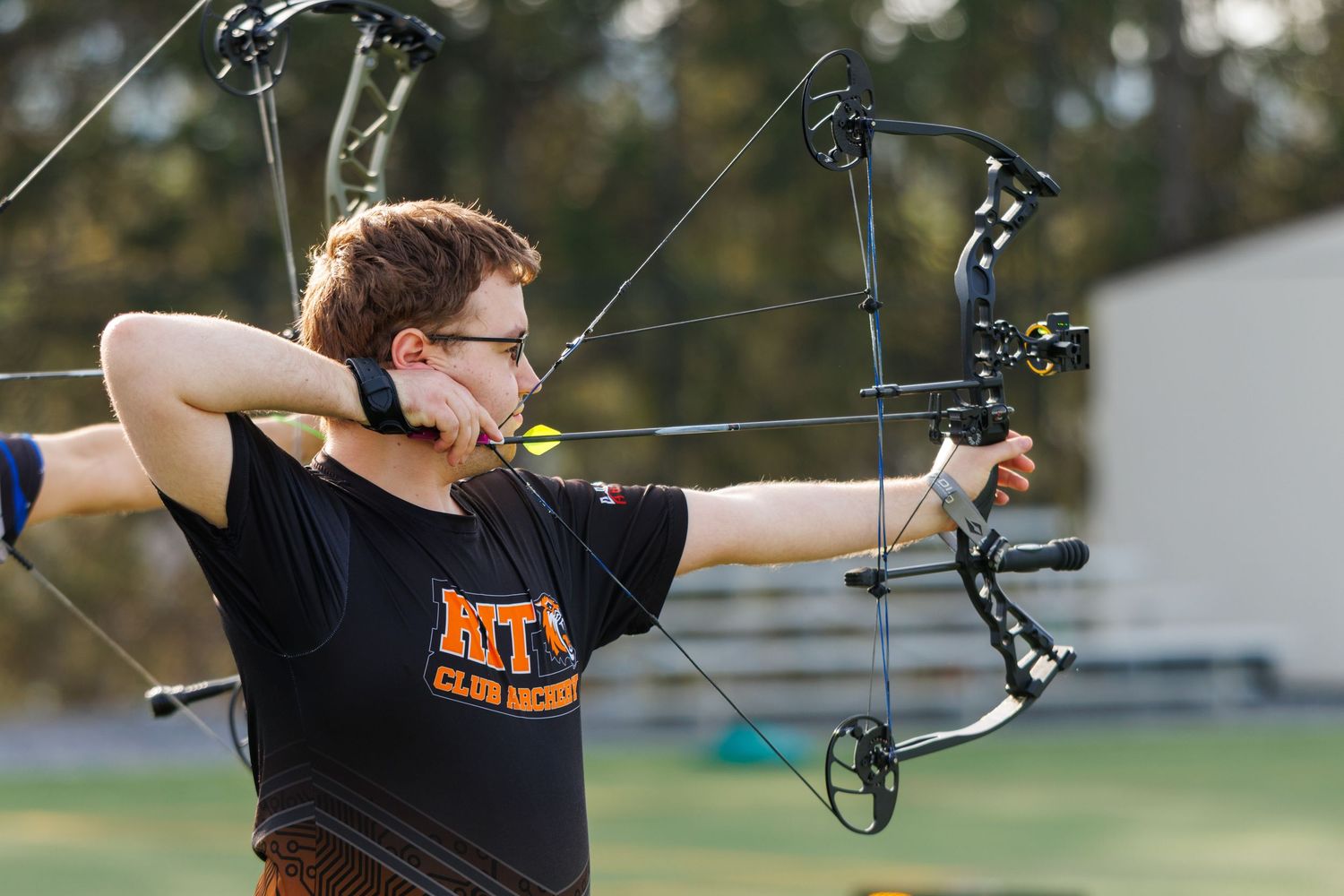Young archer in black shirt aims compound bow with precision during outdoor archery practice session.
