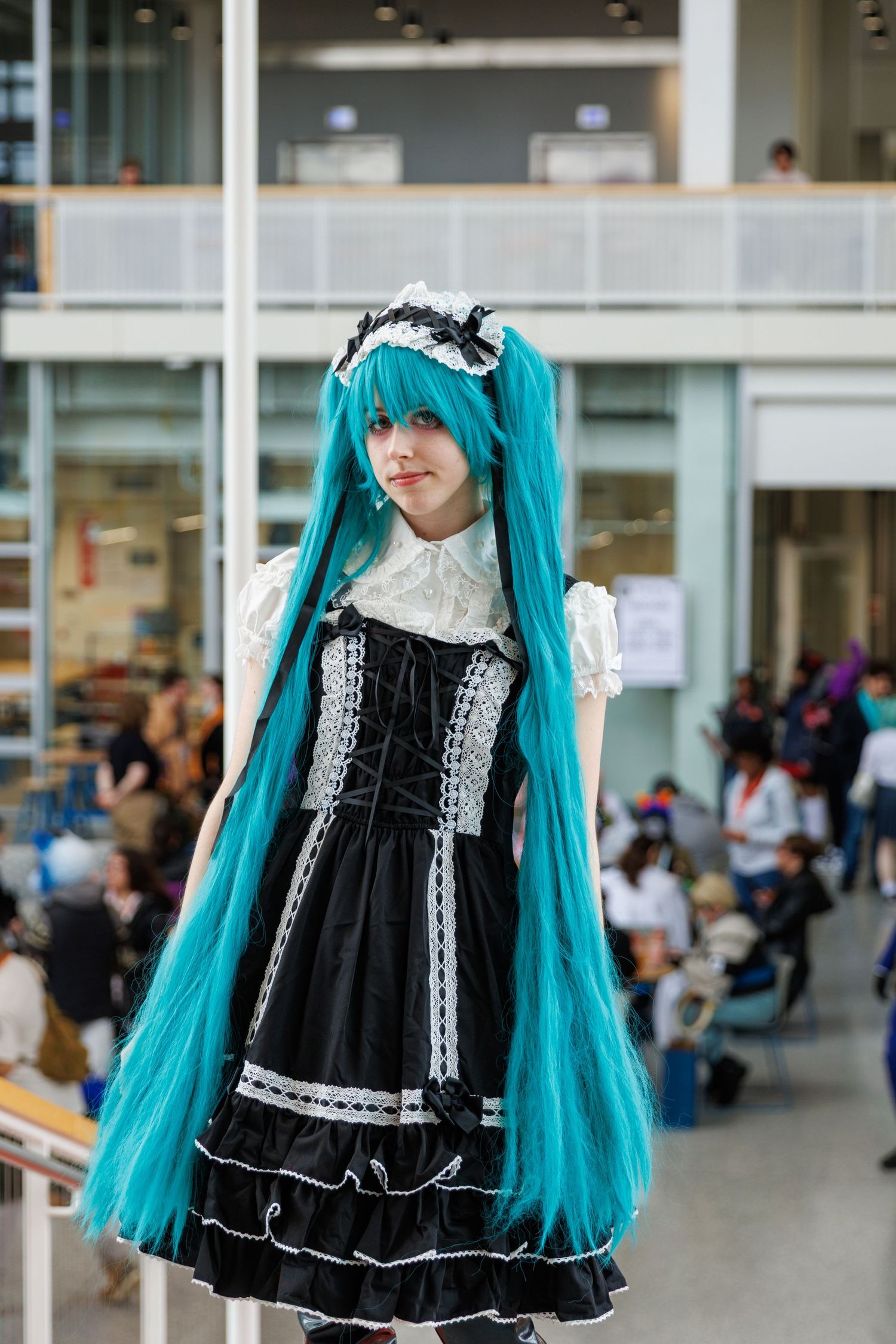 Cosplayer in black Gothic Lolita dress with long teal twin-tail wig at anime convention.