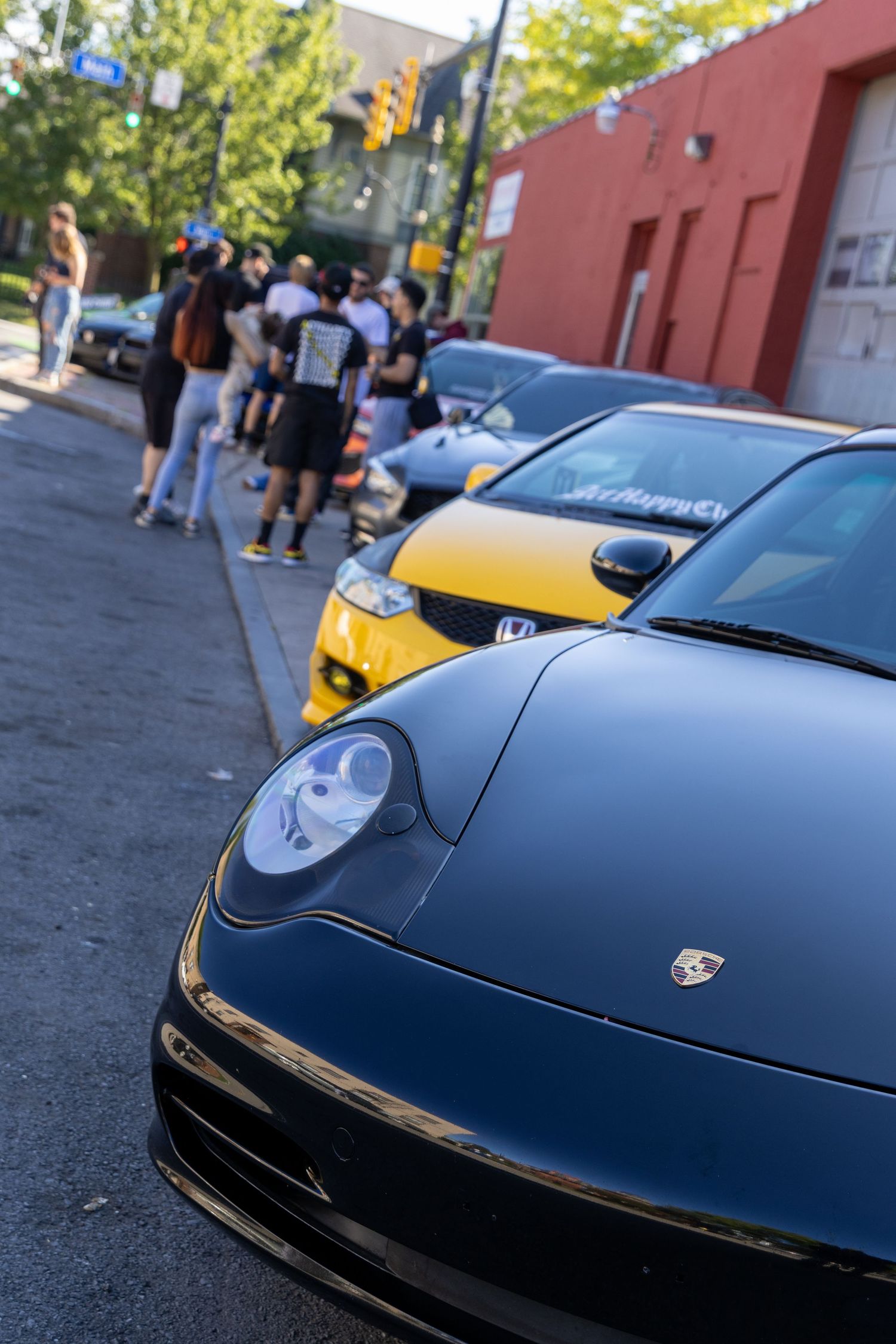 Close-up sequence of a black Porsche sports car's front hood and headlight details parked on a city street.