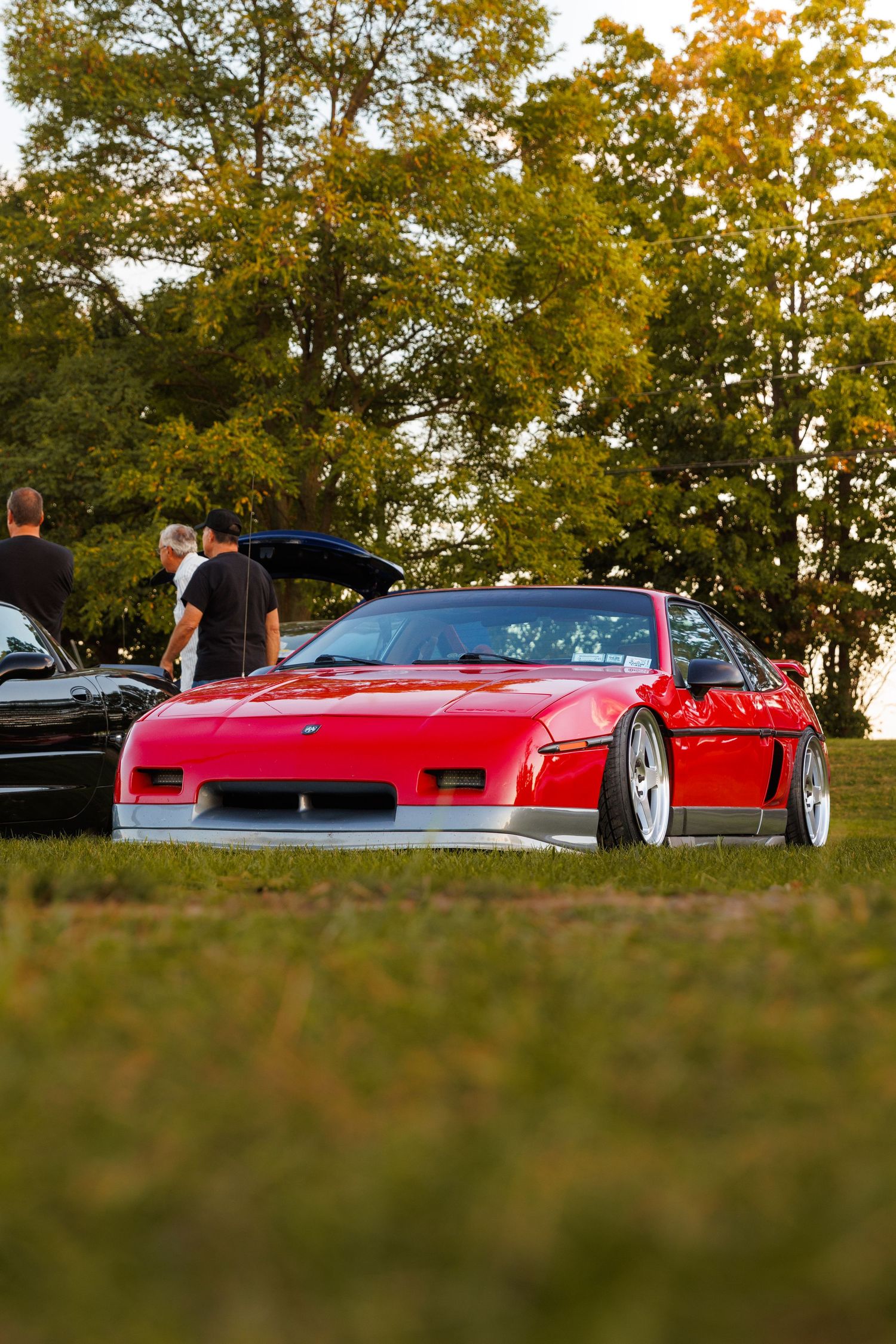 Red Ferrari F40 supercar parked on grass during golden hour with trees in background.