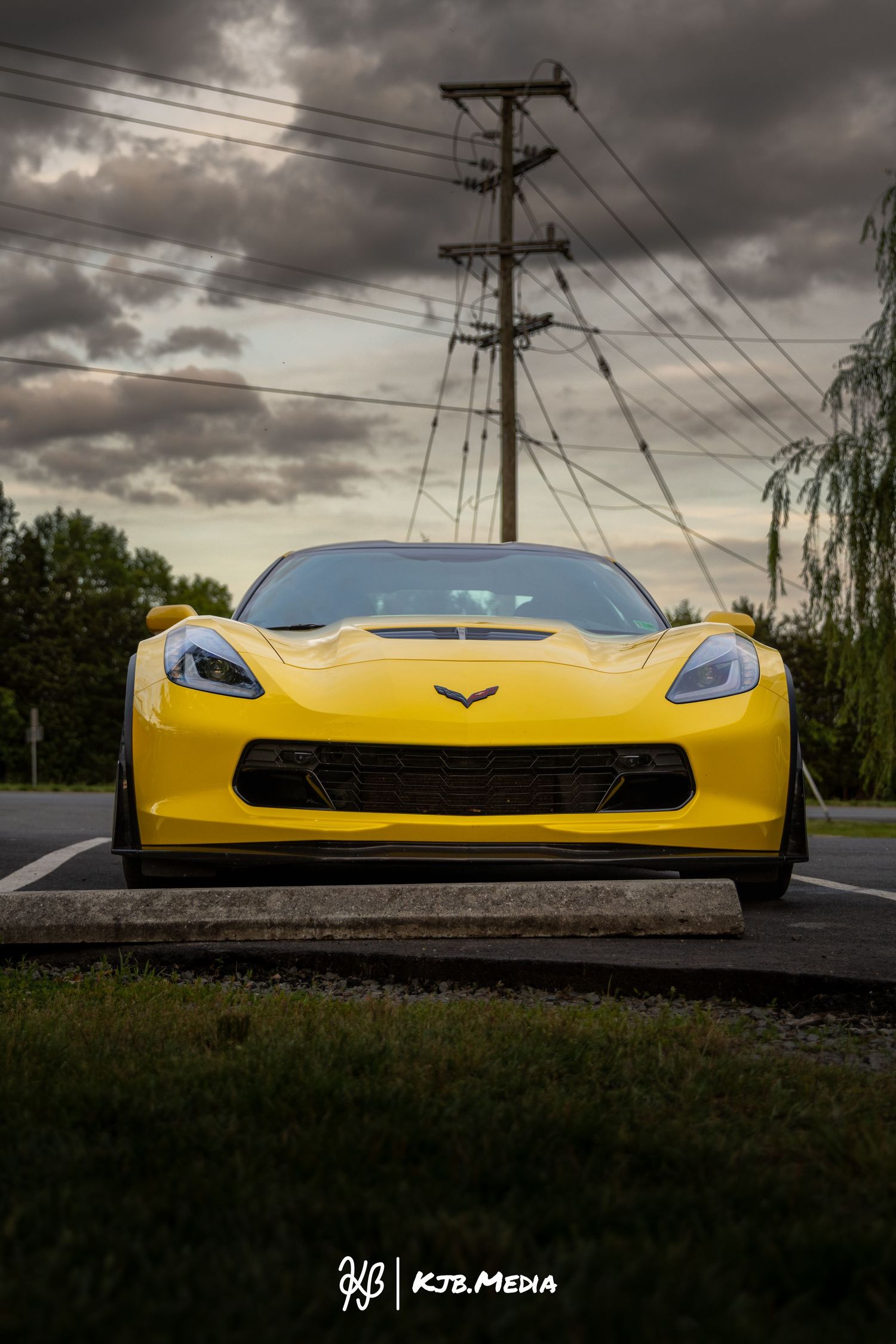 Low-angle shot of a yellow Corvette with dramatic storm clouds and power lines above.