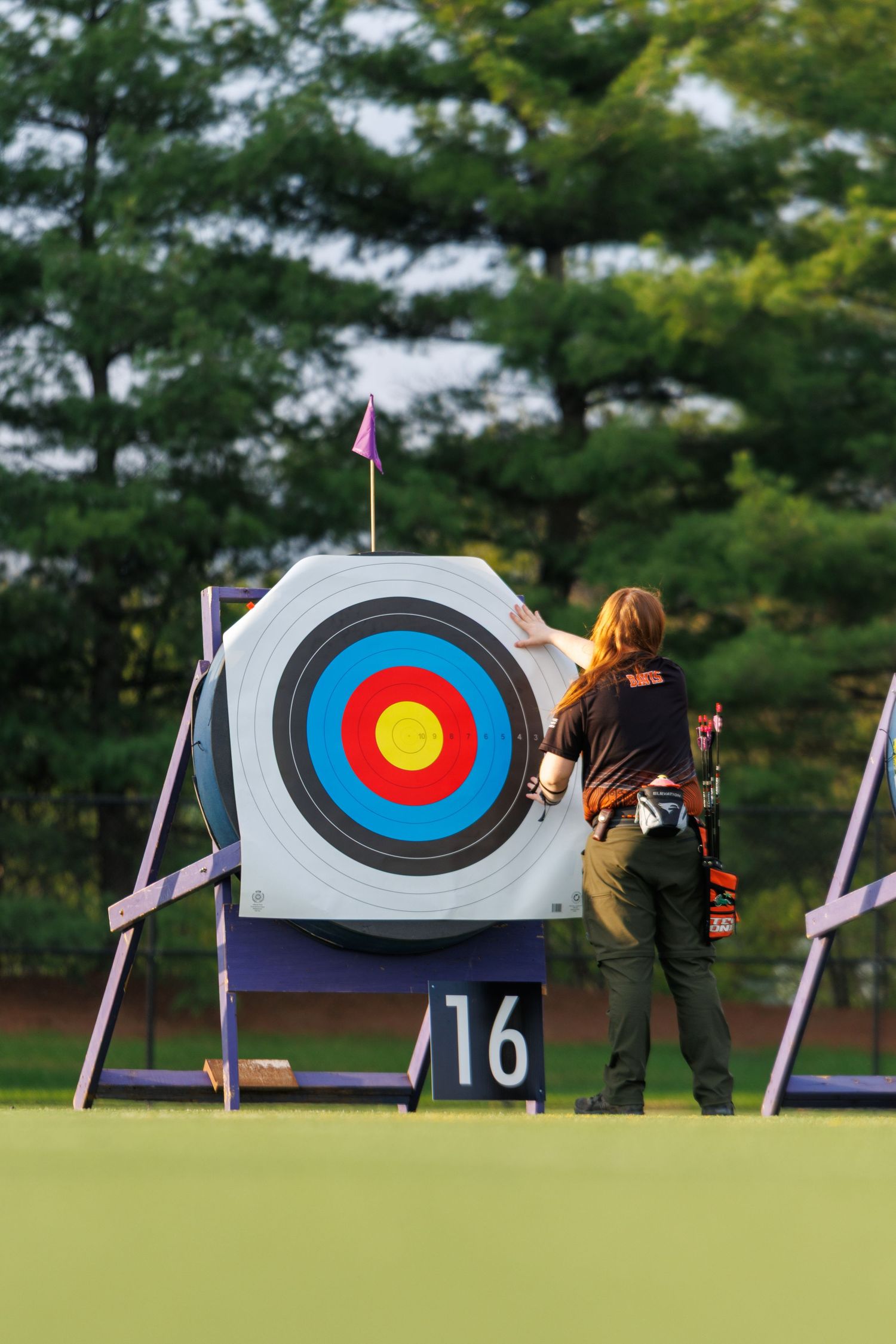 Archer retrieving arrows from a colorful target board numbered 16 at an outdoor archery competition.