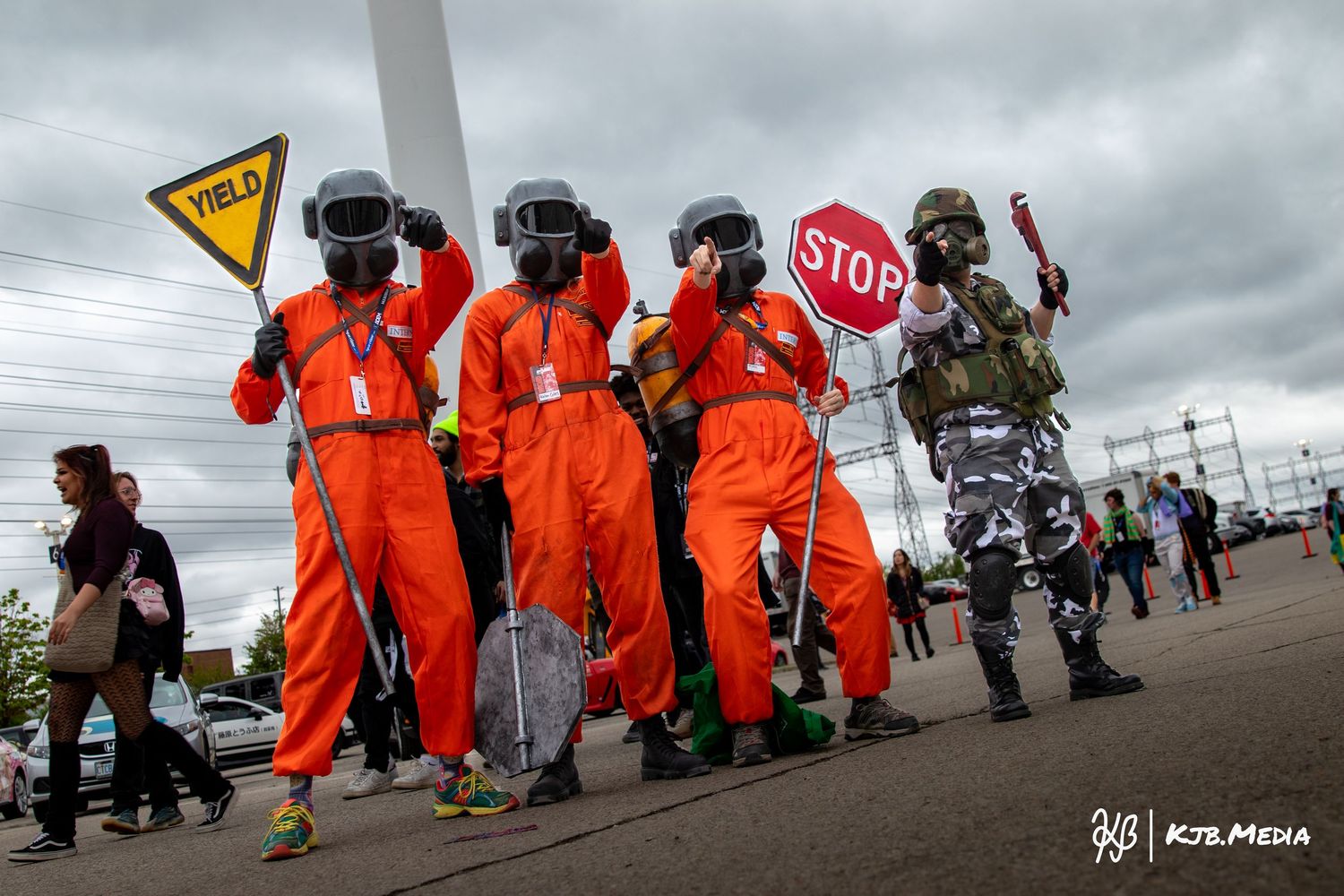 Group of cosplayers in orange jumpsuits and military gear pose with stop signs.