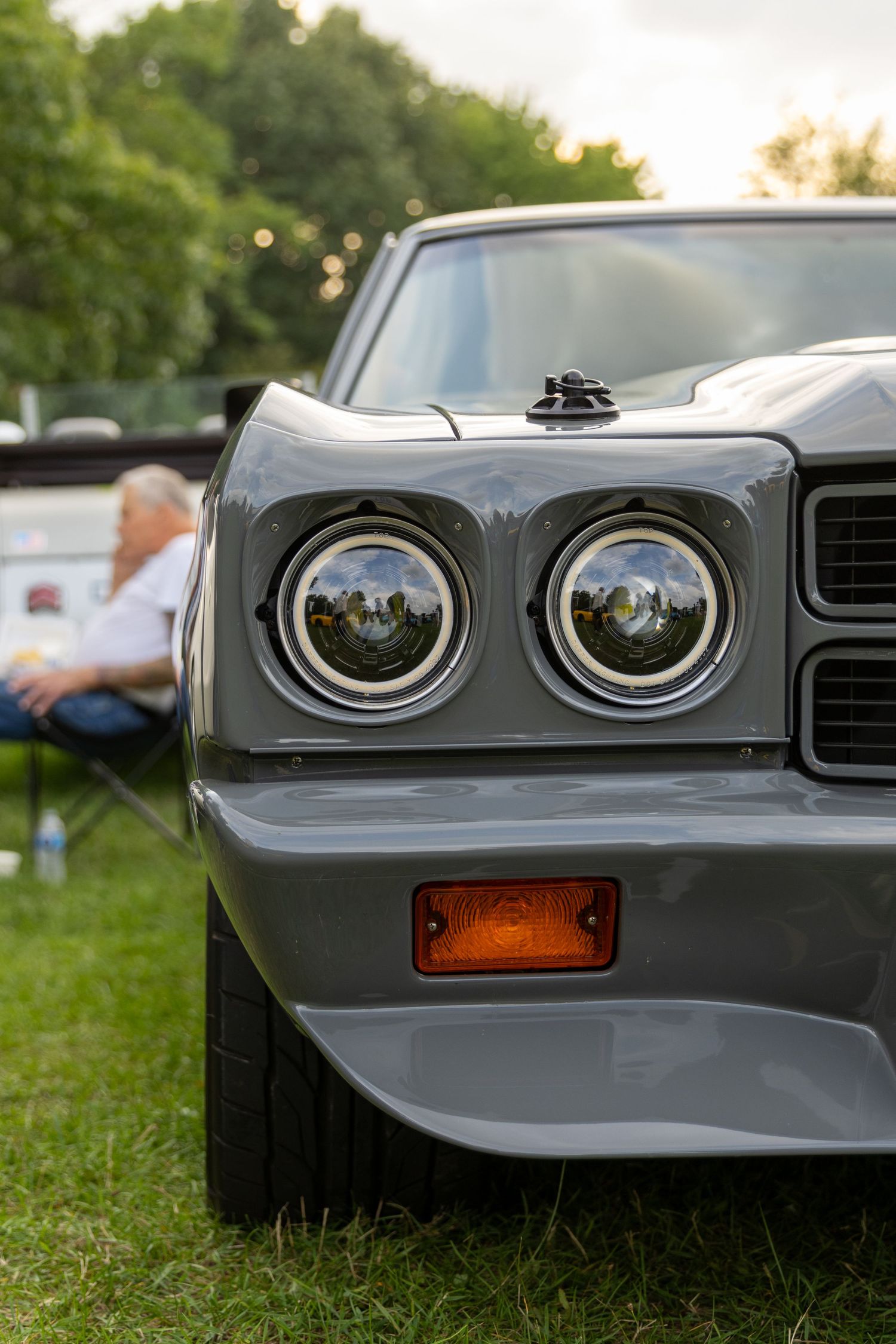Close-up view of dual round headlights and orange marker light on a classic Pontiac car's front end at an outdoor car show.