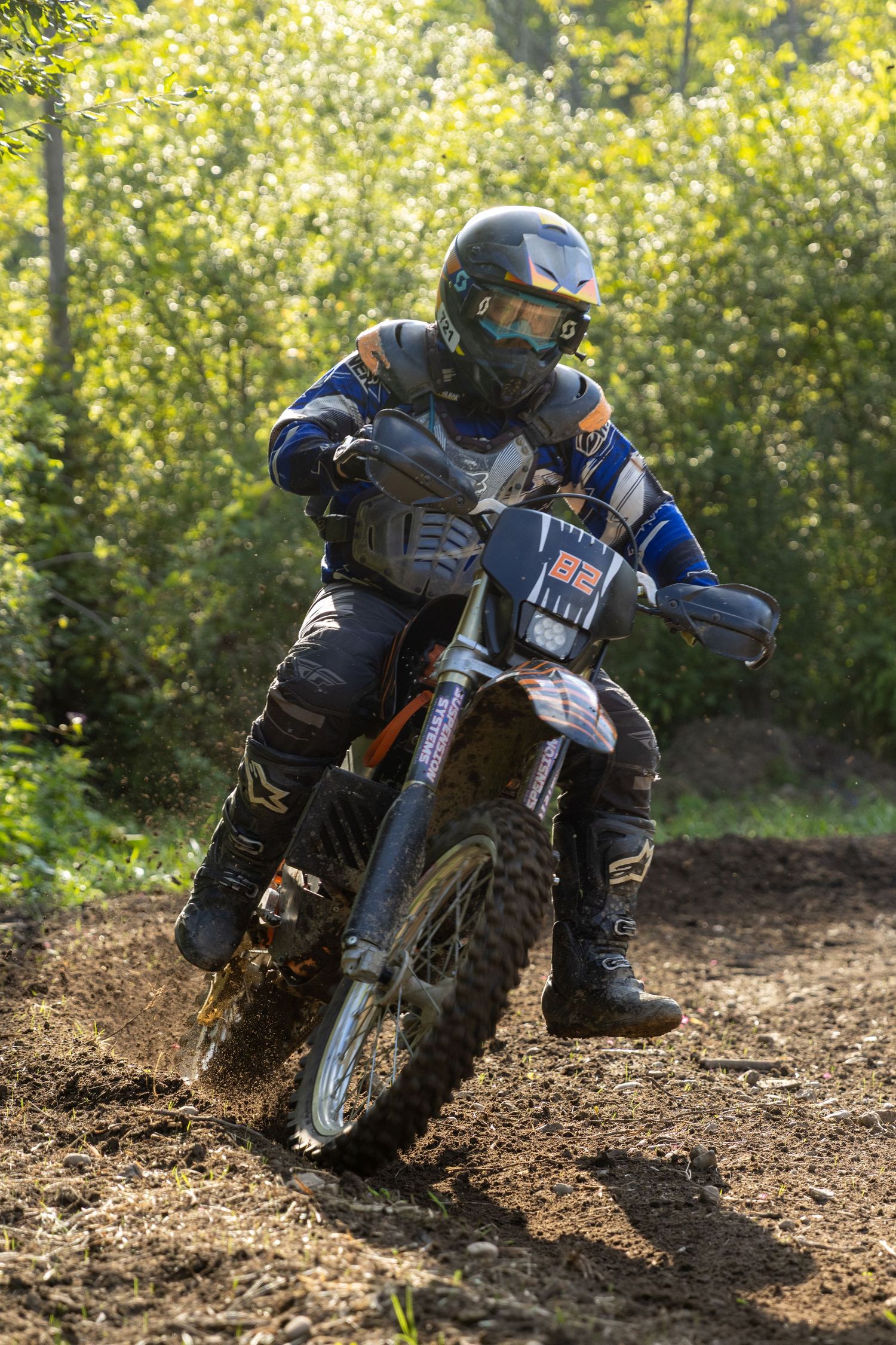 Dirt bike rider leans through challenging turn on muddy trail, kicking up soil during intense off-road action sequence.