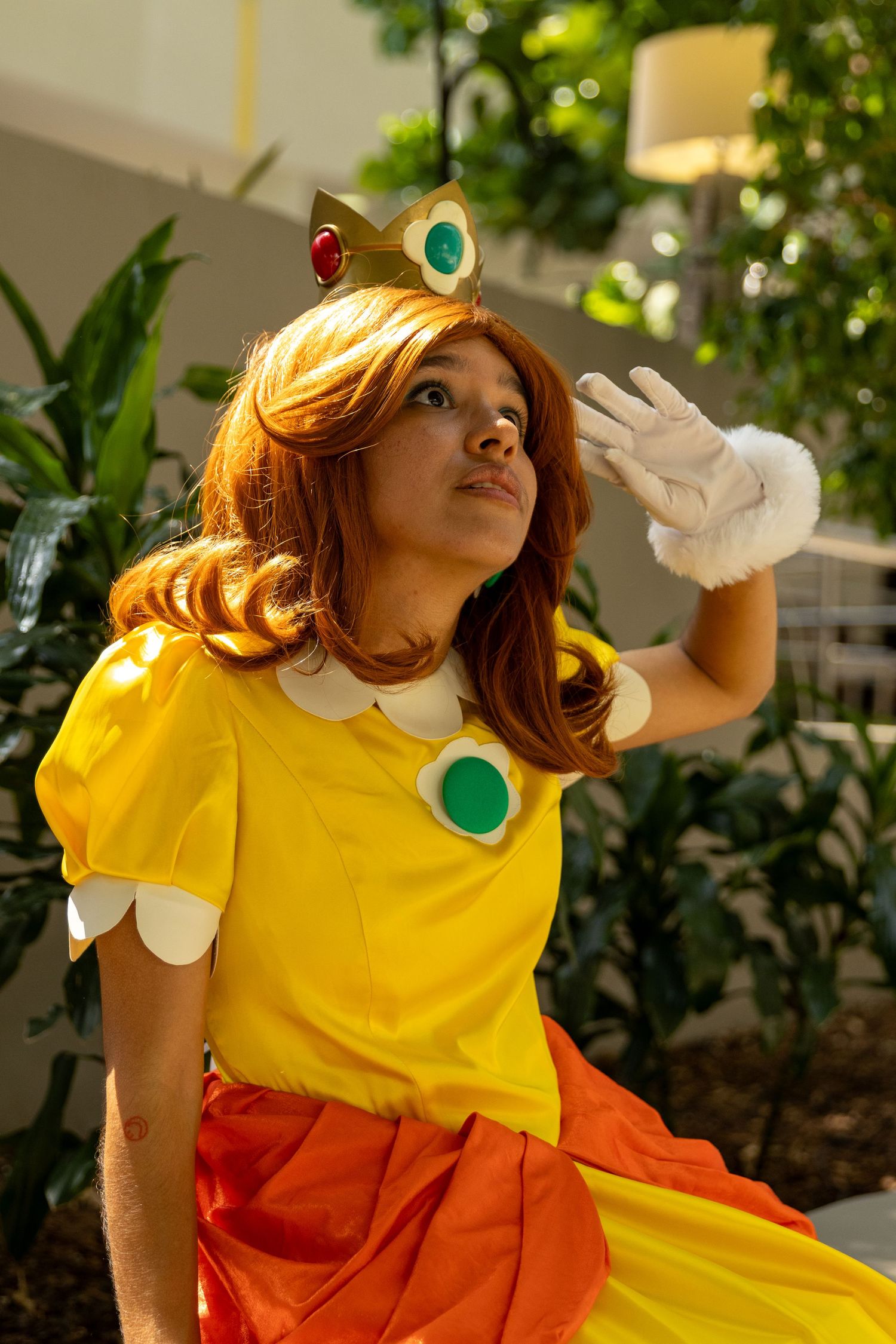 A cosplay character in a yellow and orange dress performs energetic poses against a garden backdrop.