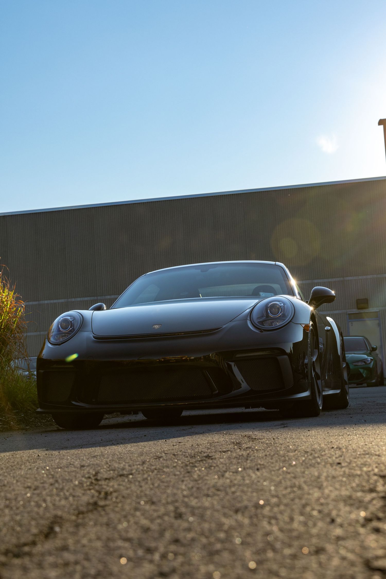 A black Porsche sports car photographed at a low angle during sunset with dramatic lighting and shadows.