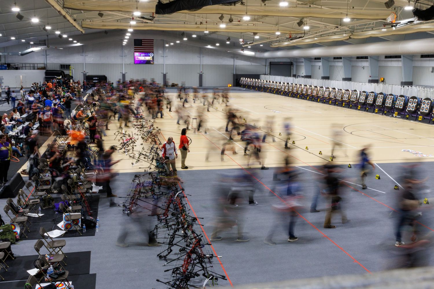 Aerial view of a large robotics competition event with teams and robots filling a spacious convention hall.