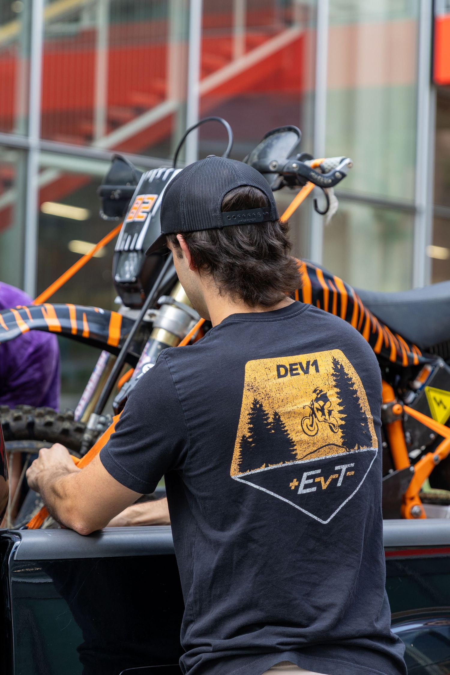 Mountain biker wearing a black t-shirt with Devi logo and forest scene design on the back.