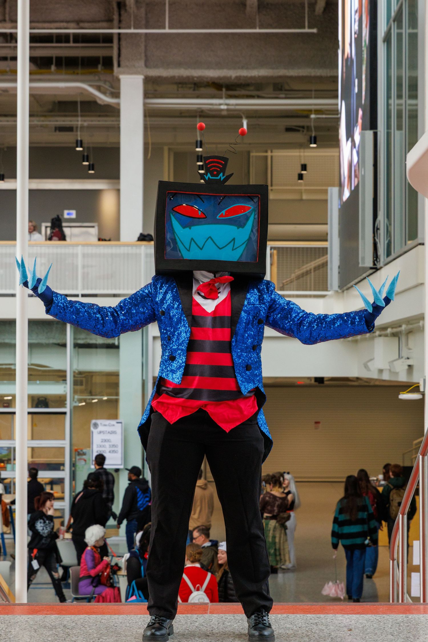 Person in blue sequin jacket and TV head costume with claws at a cosplay convention.