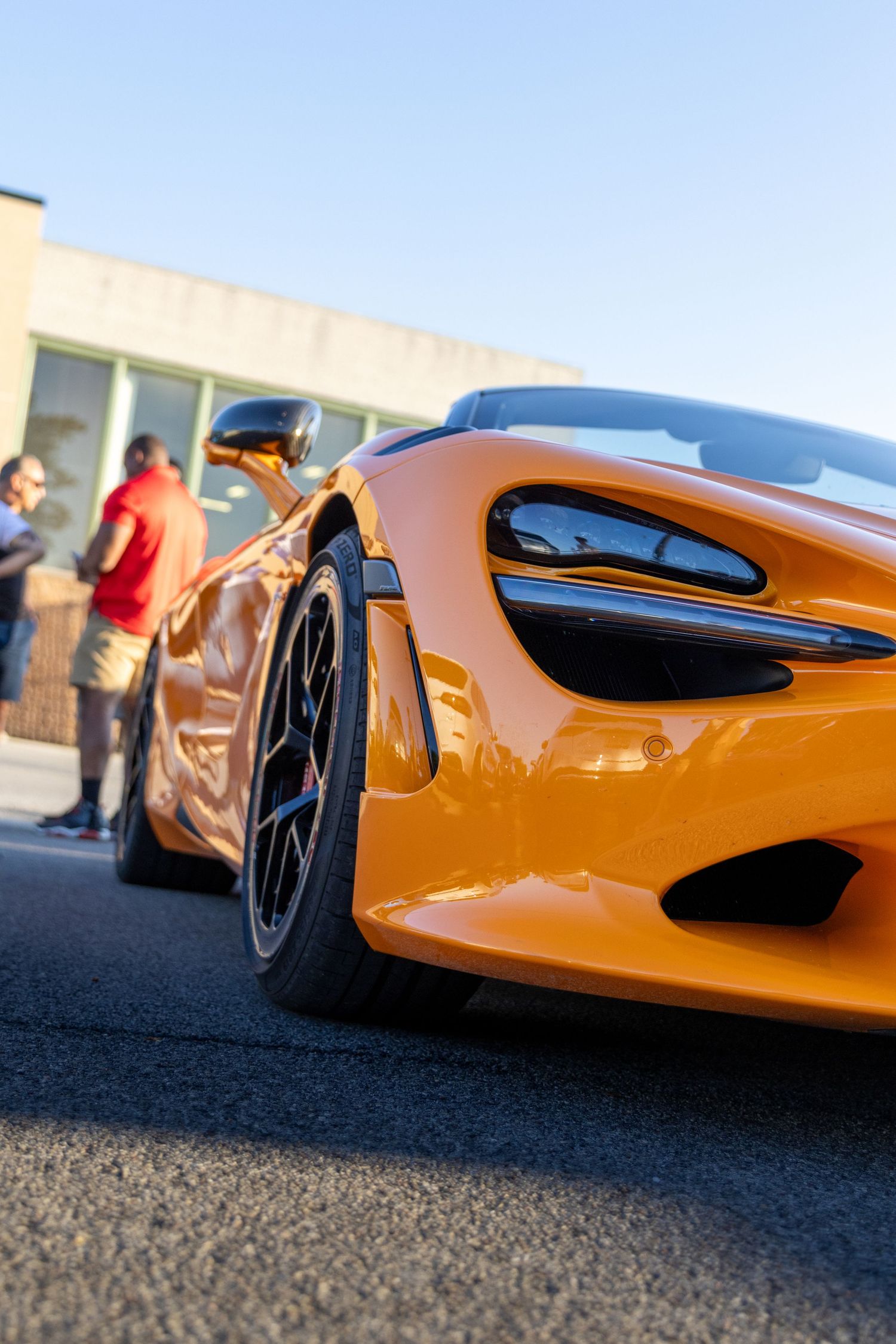 Close-up view of an orange McLaren supercar's aerodynamic side profile and wheels against asphalt pavement.