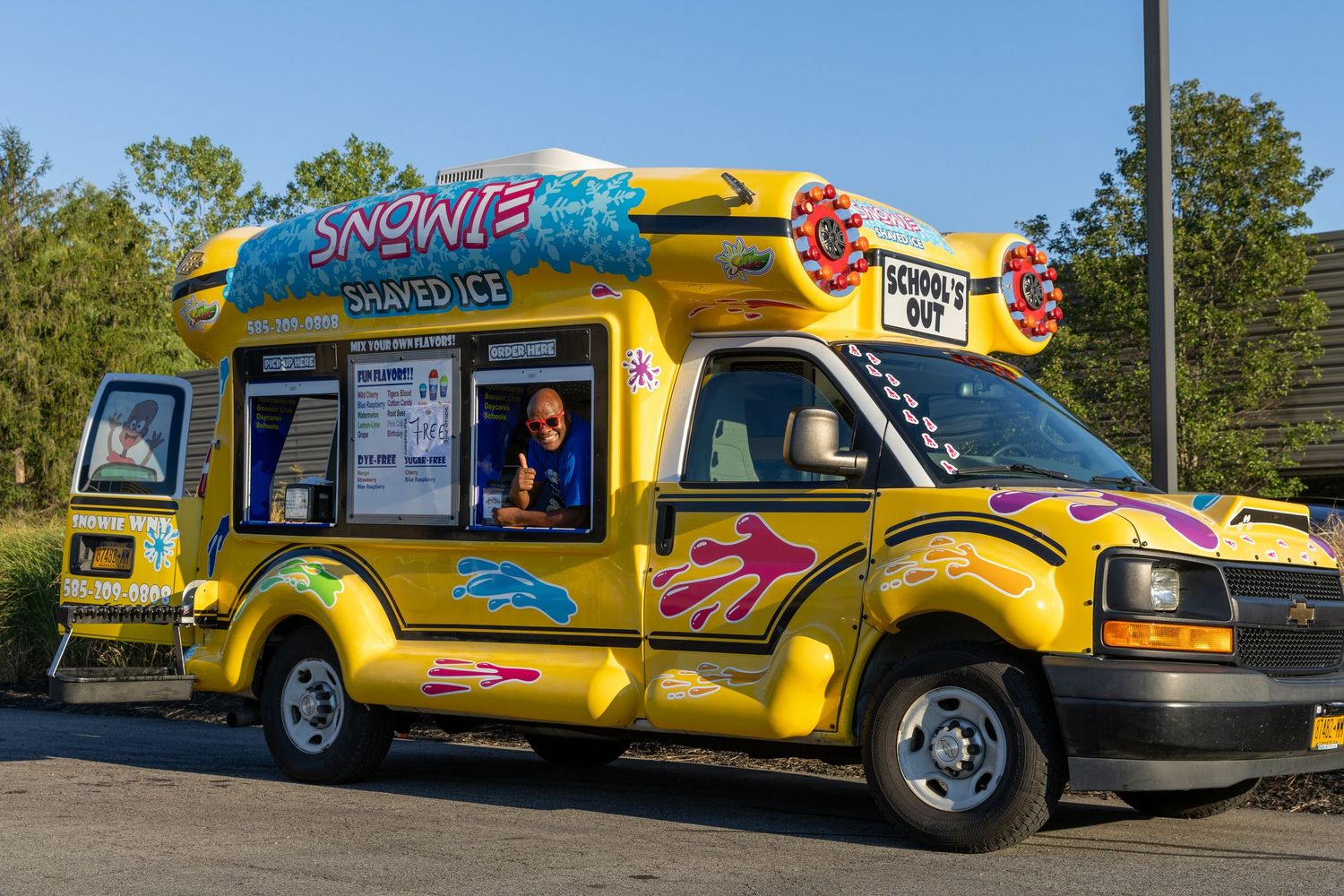 A lineup of customized yellow ice cream and snack trucks with colorful graphics and designs parked outdoors during daytime.