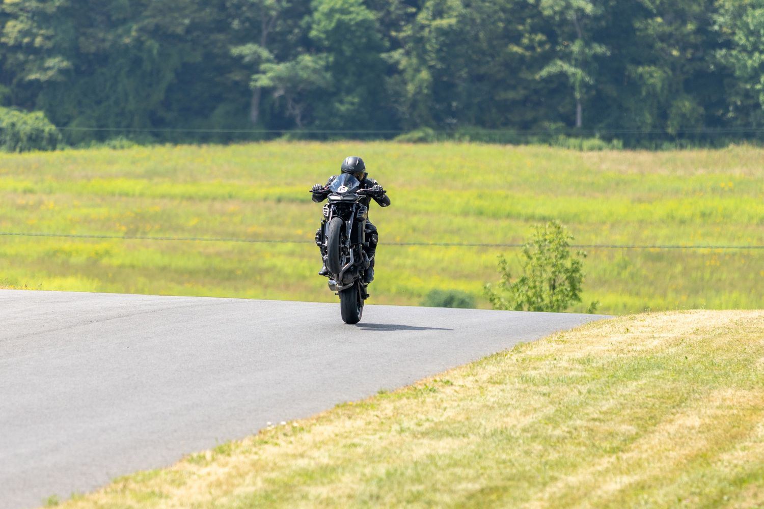A motorcyclist rides on a winding rural road through scenic countryside with lush green hills and trees.