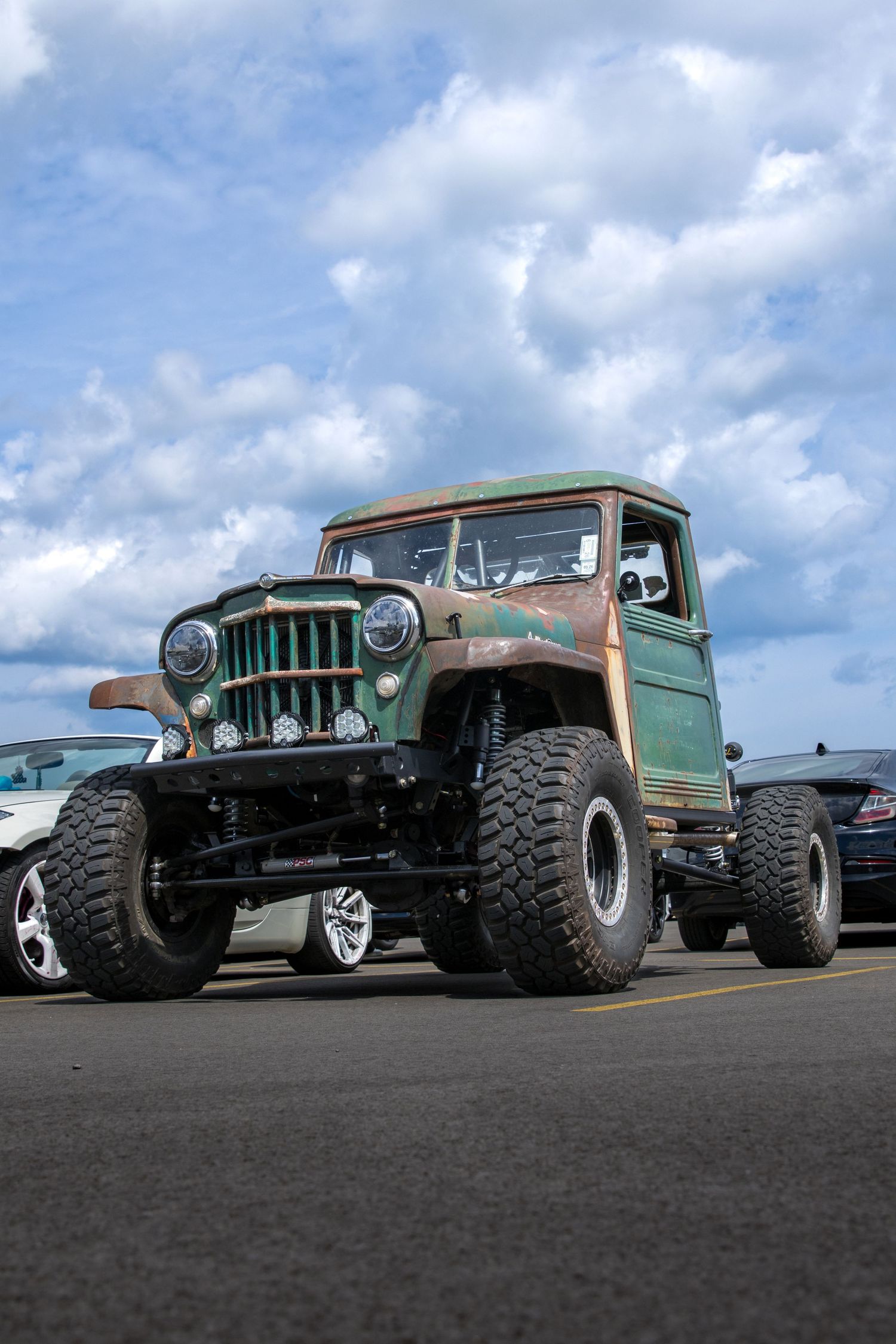 Row of customized vintage Jeeps with large off-road tires and rugged modifications parked against a cloudy sky backdrop.