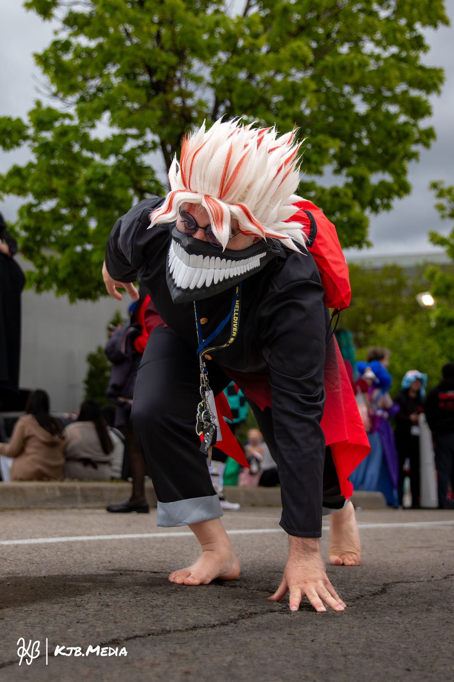 Cosplayer in a dramatic crouching pose with spiky white and red hair.