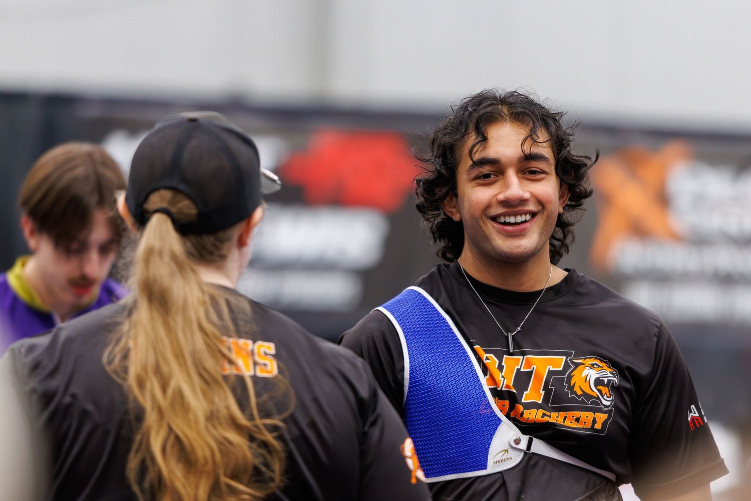 Young athlete in black and blue sports jersey smiling at an outdoor sporting event.