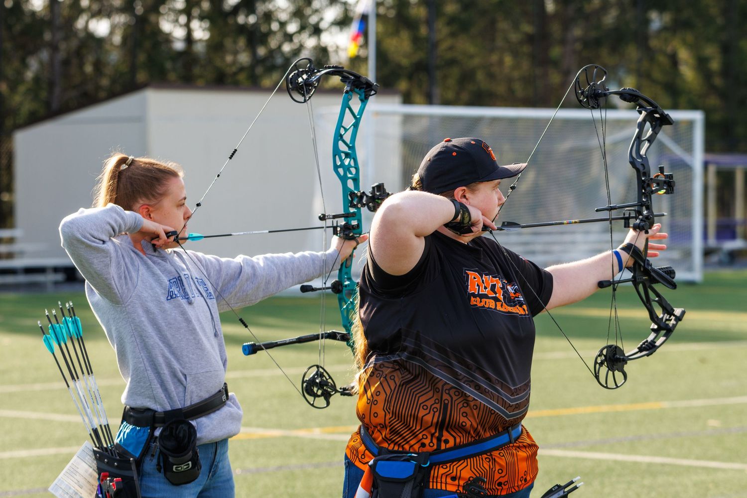 Two female archers practicing with compound bows on an outdoor field during an archery competition.