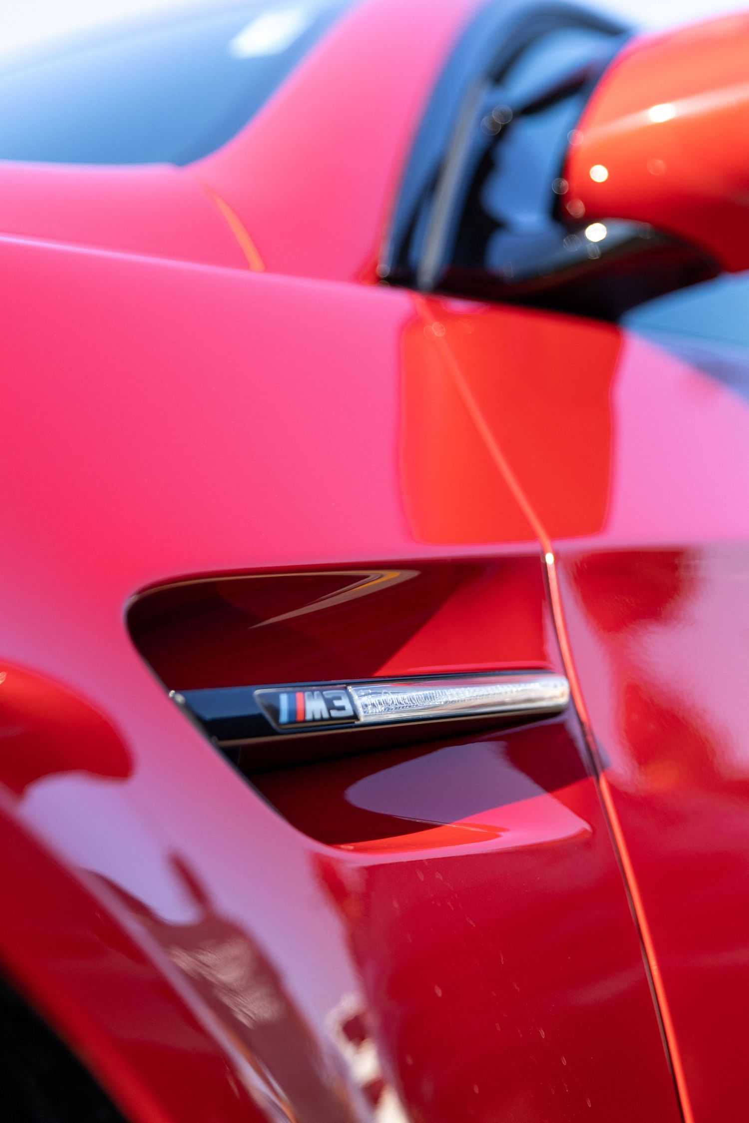 Close-up detail shot of a red BMW M3 side vent badge.