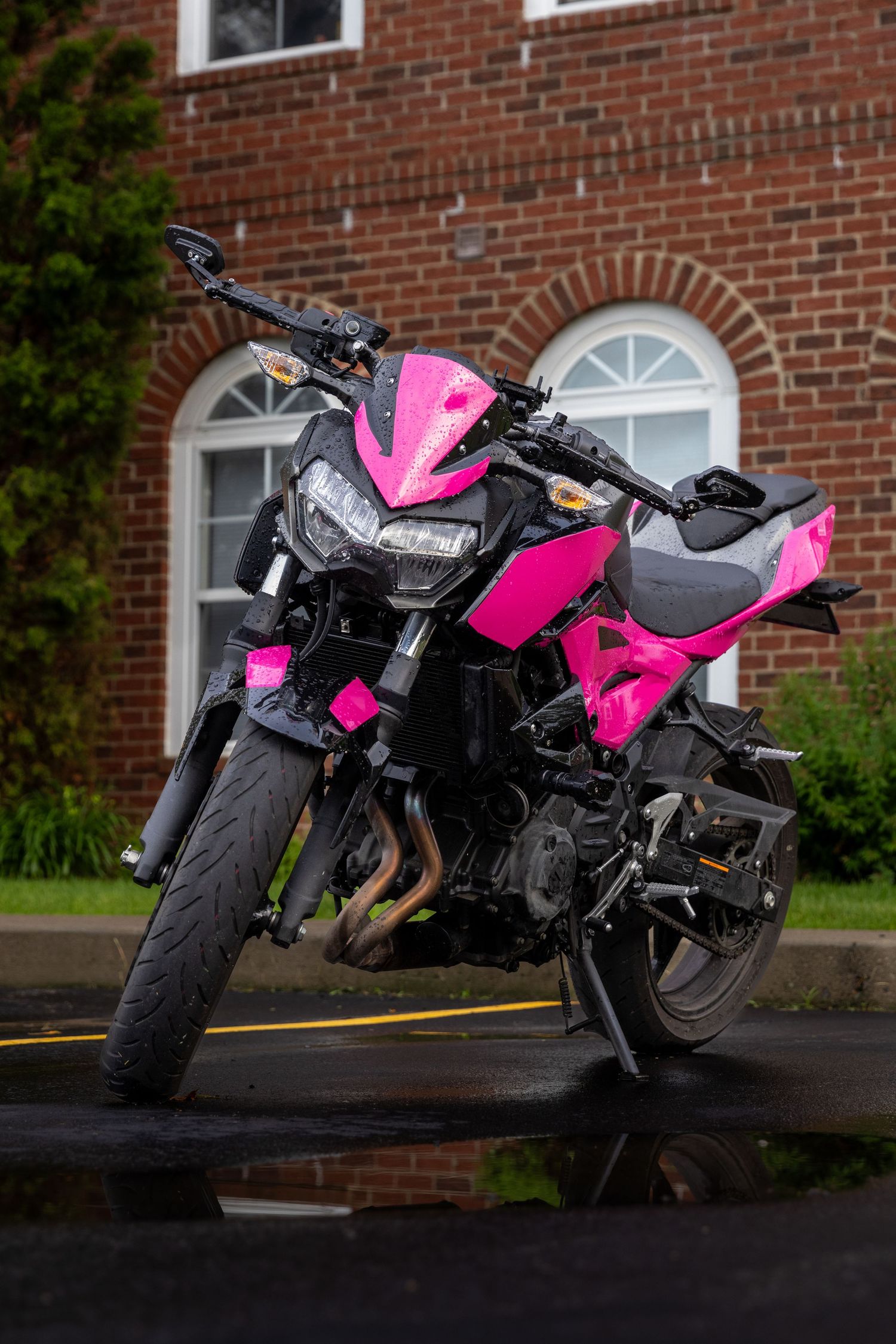 Black and pink Kawasaki motorcycle parked in front of brick building.